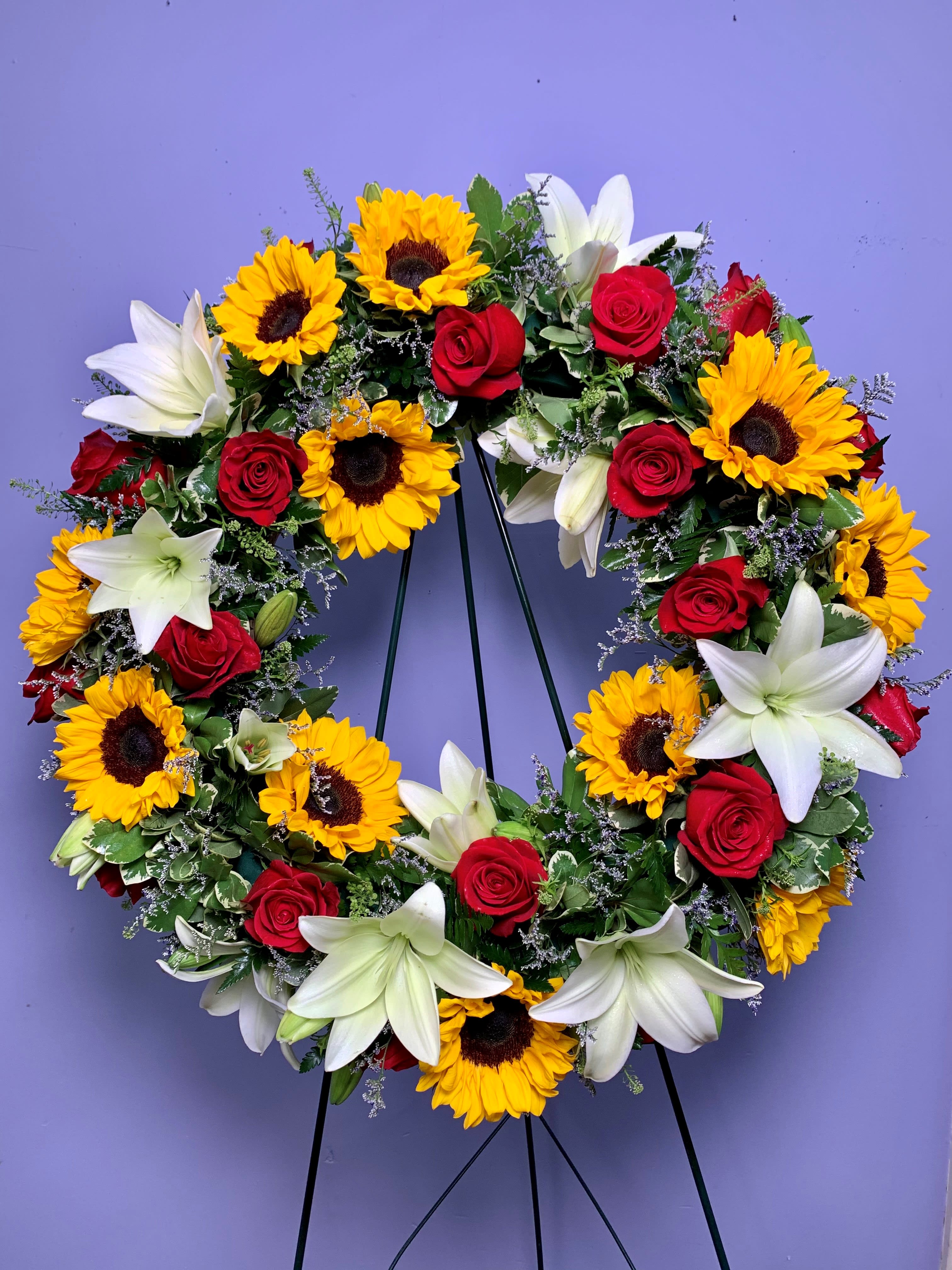 Circular wreath of red roses, white lilies, and yellow sunflowers on a stand