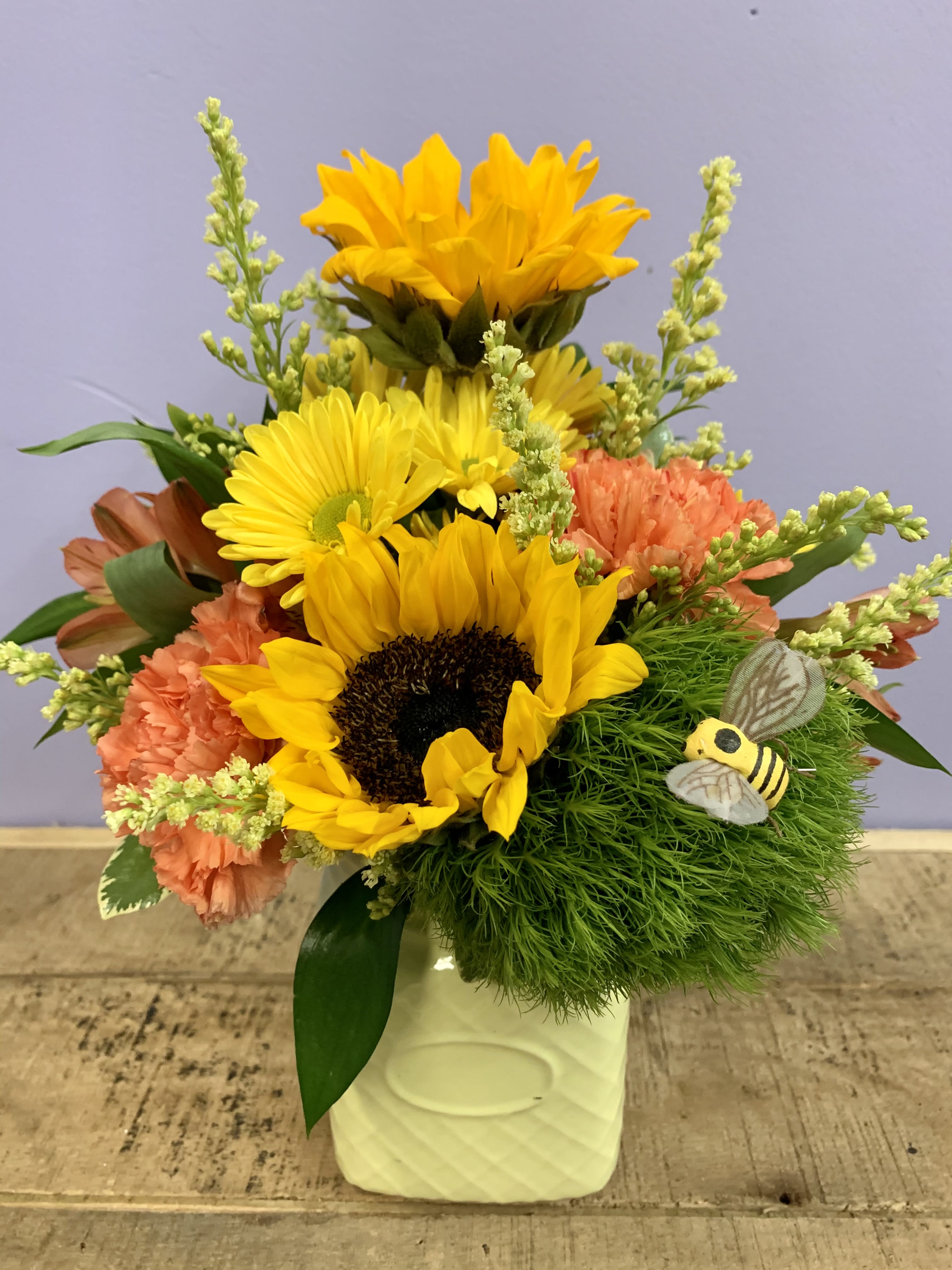 Sunflower and carnation arrangement in a white vase with a bee decoration
