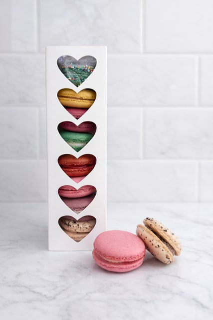 Box of assorted heart-shaped macarons with two macarons in front