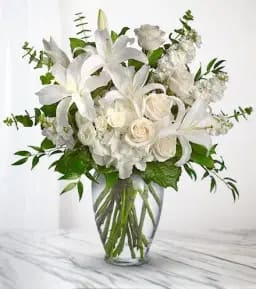 White lilies and roses in a clear glass vase with greenery