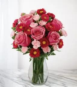 Pink roses and red daisy-like flowers arranged in a clear glass vase