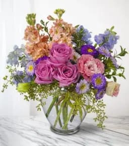 Mixed bouquet of pink roses and purple flowers in a clear glass vase
