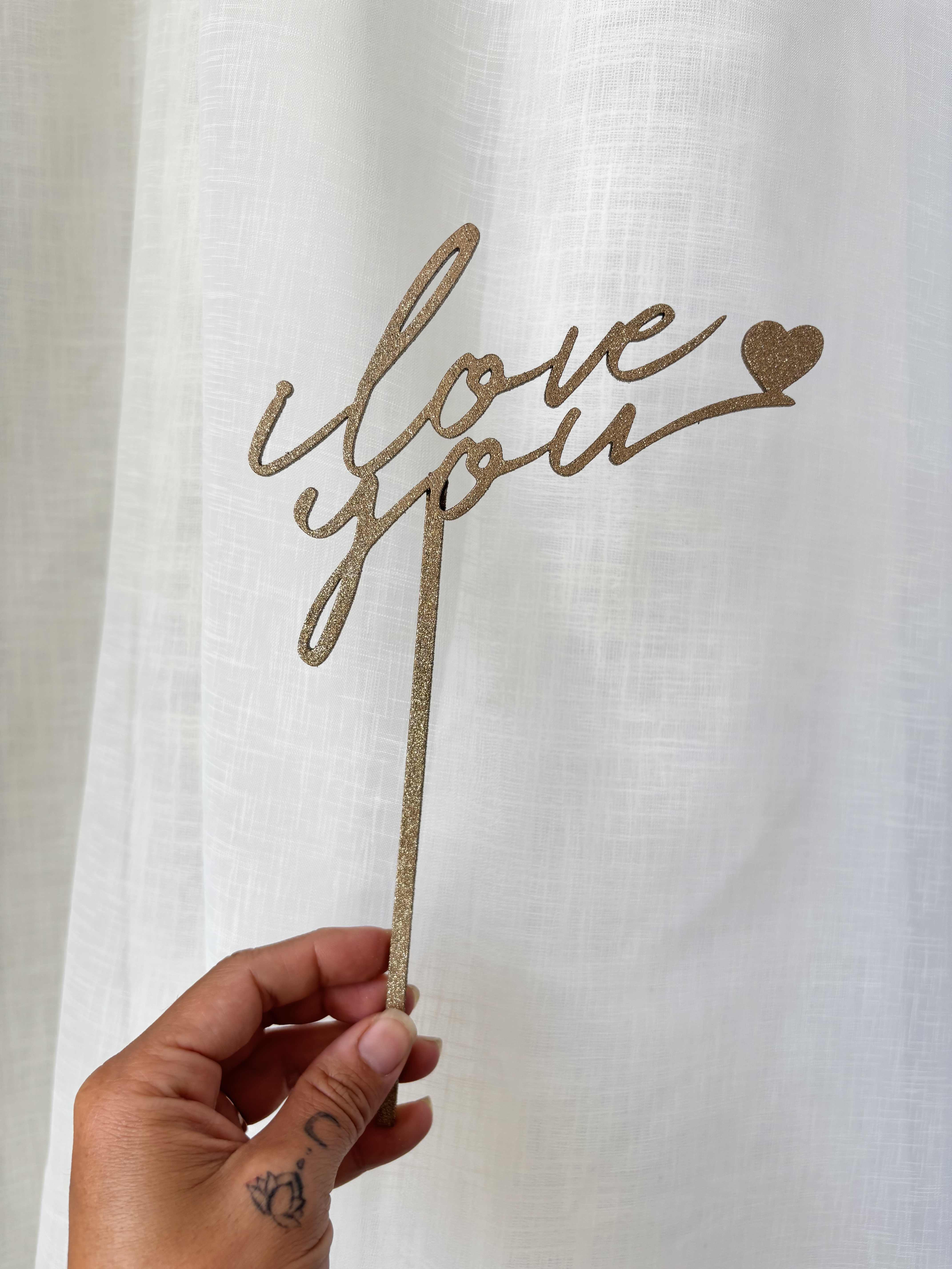 Hand holding a glittery gold "love you" cake topper