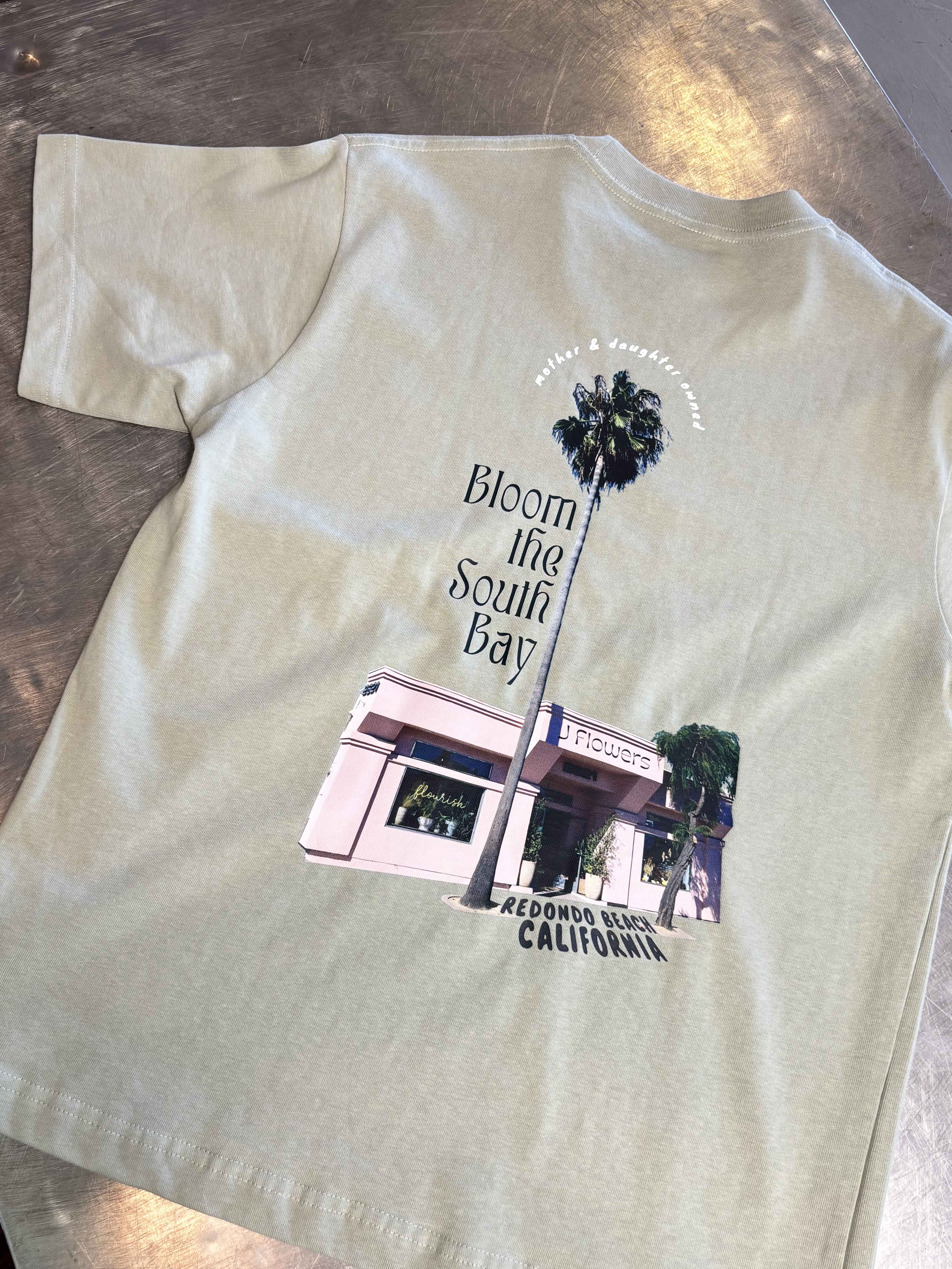 Light green T-shirt with a floral shop graphic and palm tree print