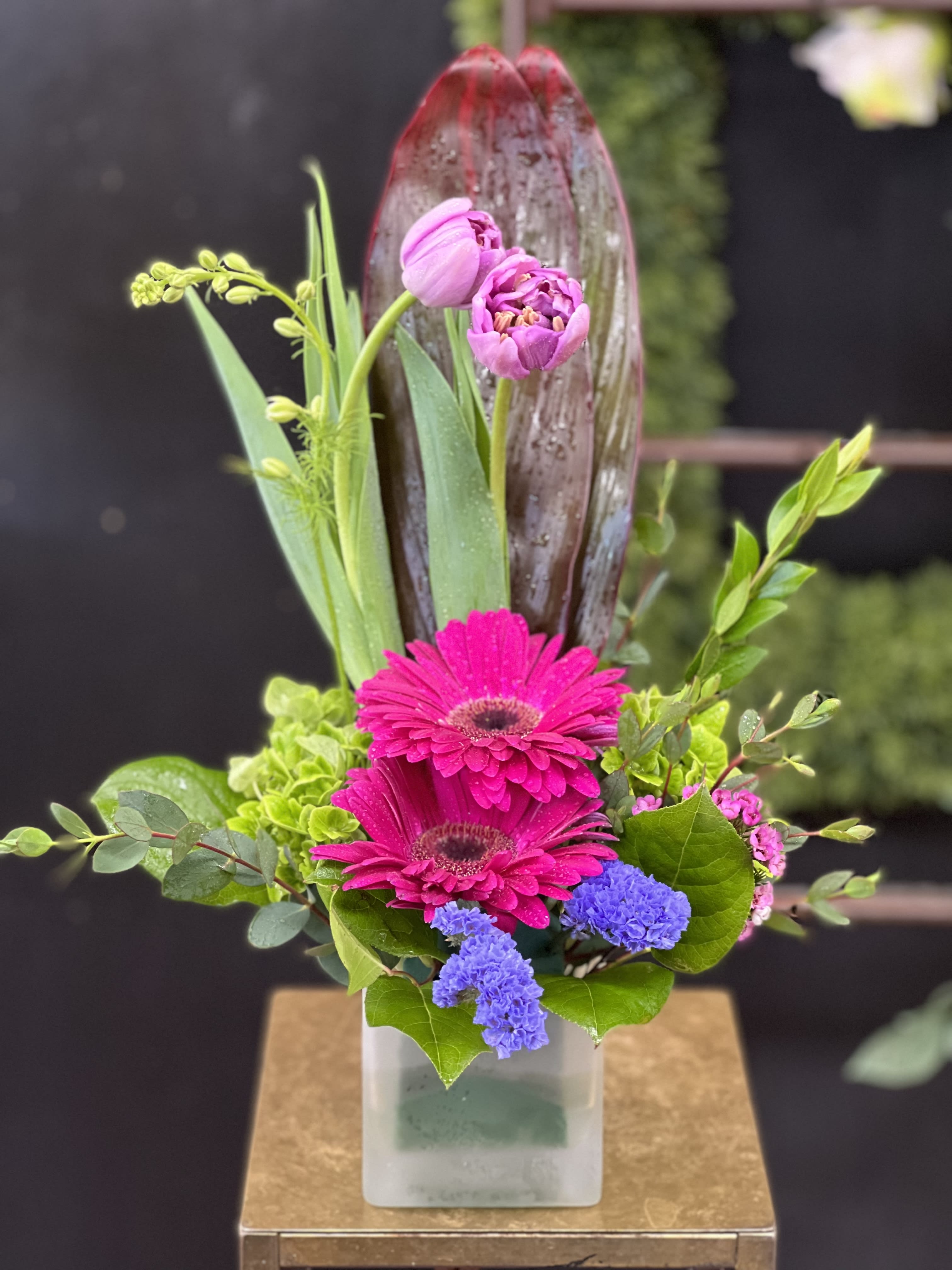 Pink gerbera daisies and tulips in a square vase with mixed greenery