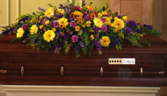 Large floral spray on a wooden casket with yellow and purple flowers