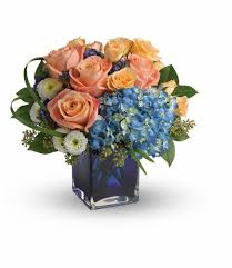 Bouquet of peach roses and blue hydrangeas in a square glass vase