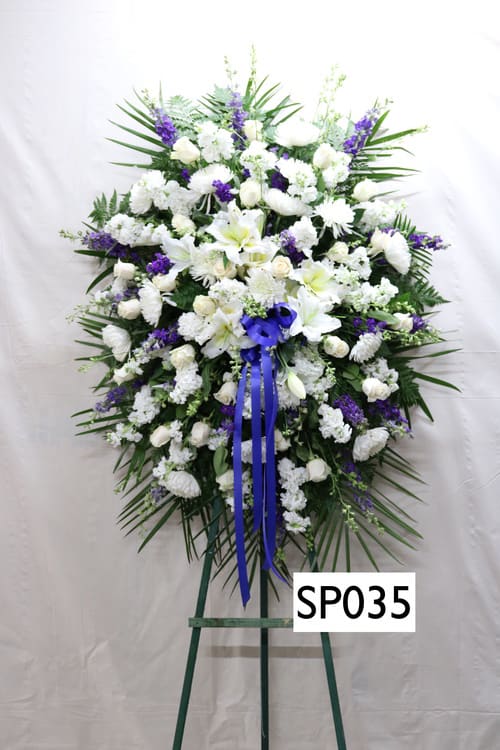 Large white and purple funeral spray on an easel with a blue ribbon