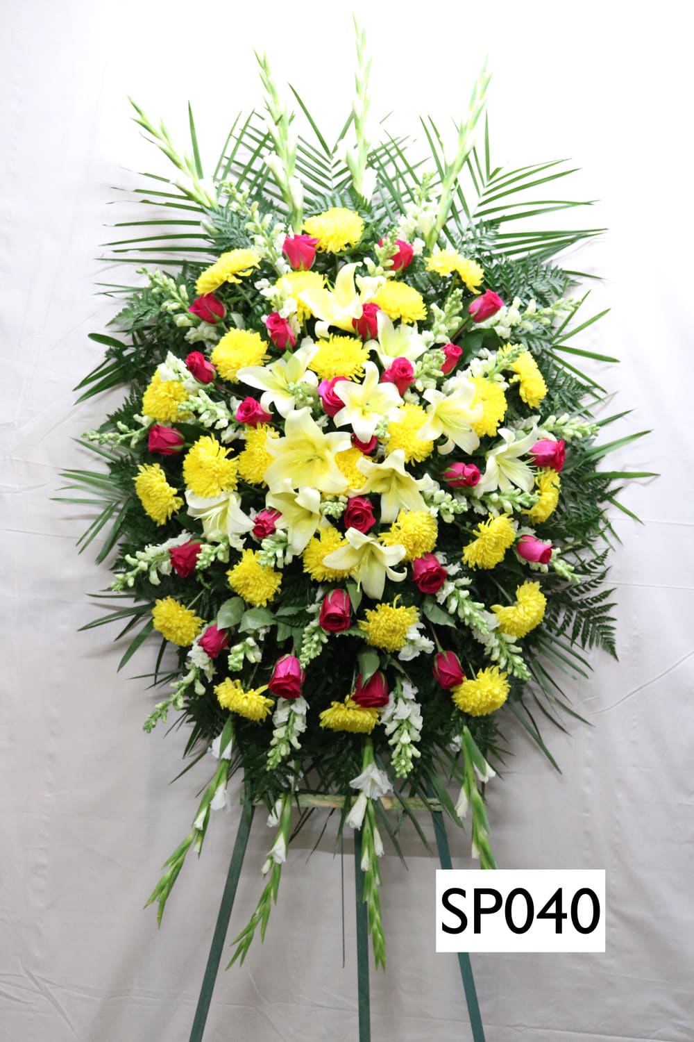 Standing funeral spray with yellow lilies, pink roses, and white blooms