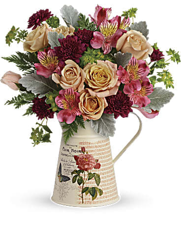 Bouquet of peach roses and burgundy flowers in a decorative pitcher vase