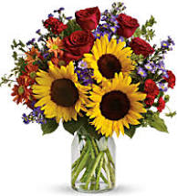 Bouquet of sunflowers, red roses, and purple flowers in a glass vase