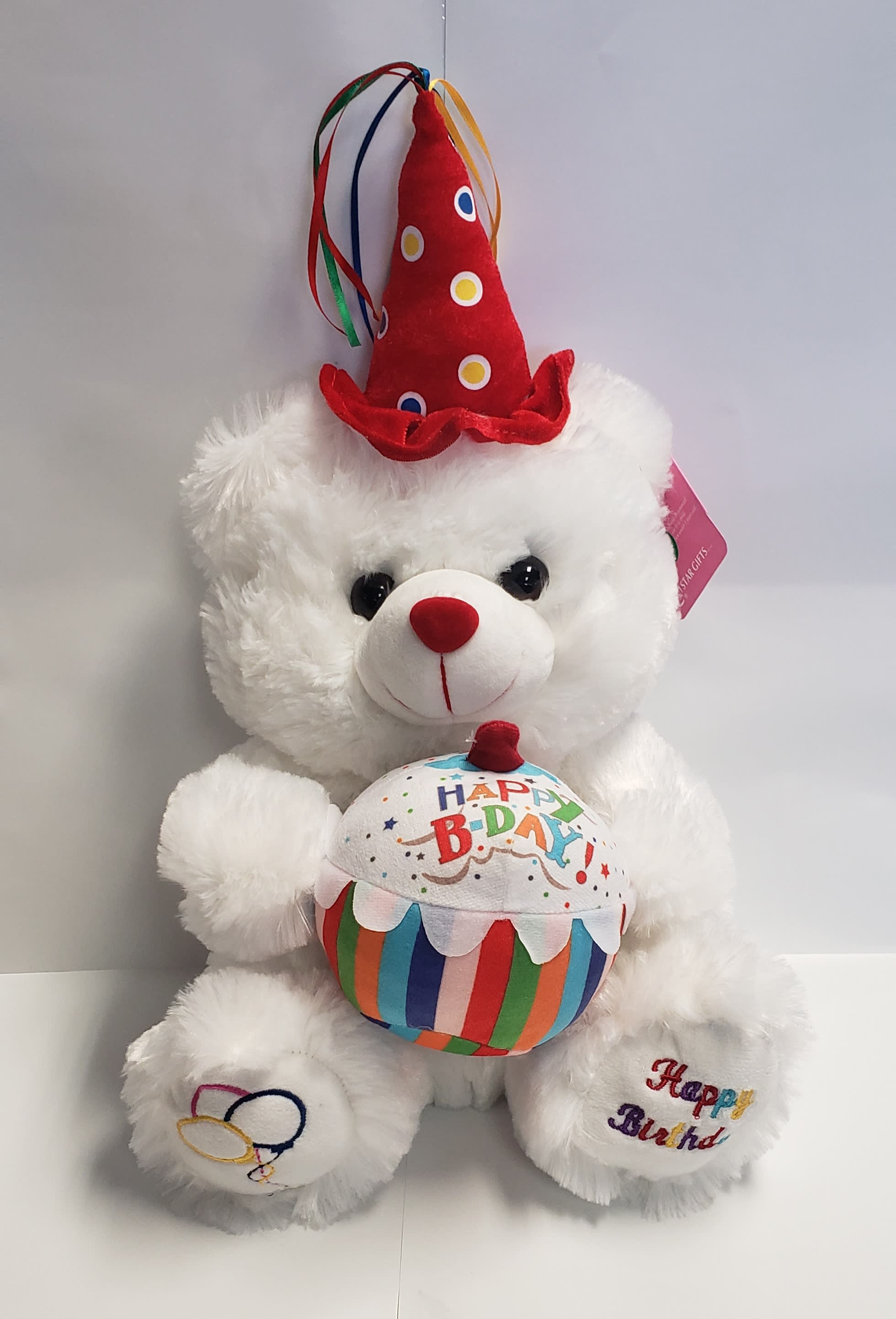 White teddy bear wearing a red birthday hat and holding a birthday cake