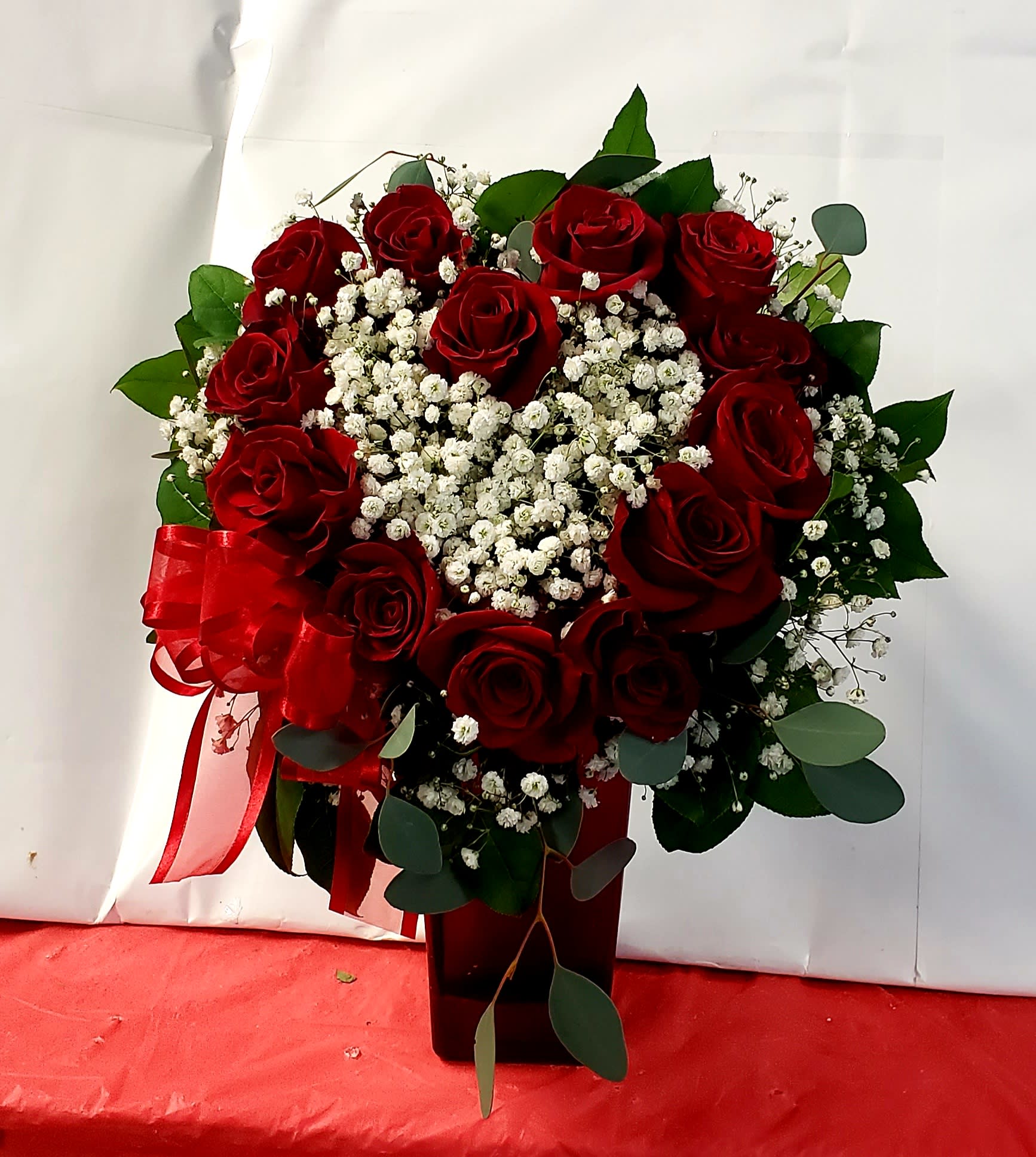 Red roses and white baby's breath in a dark vase with a red ribbon