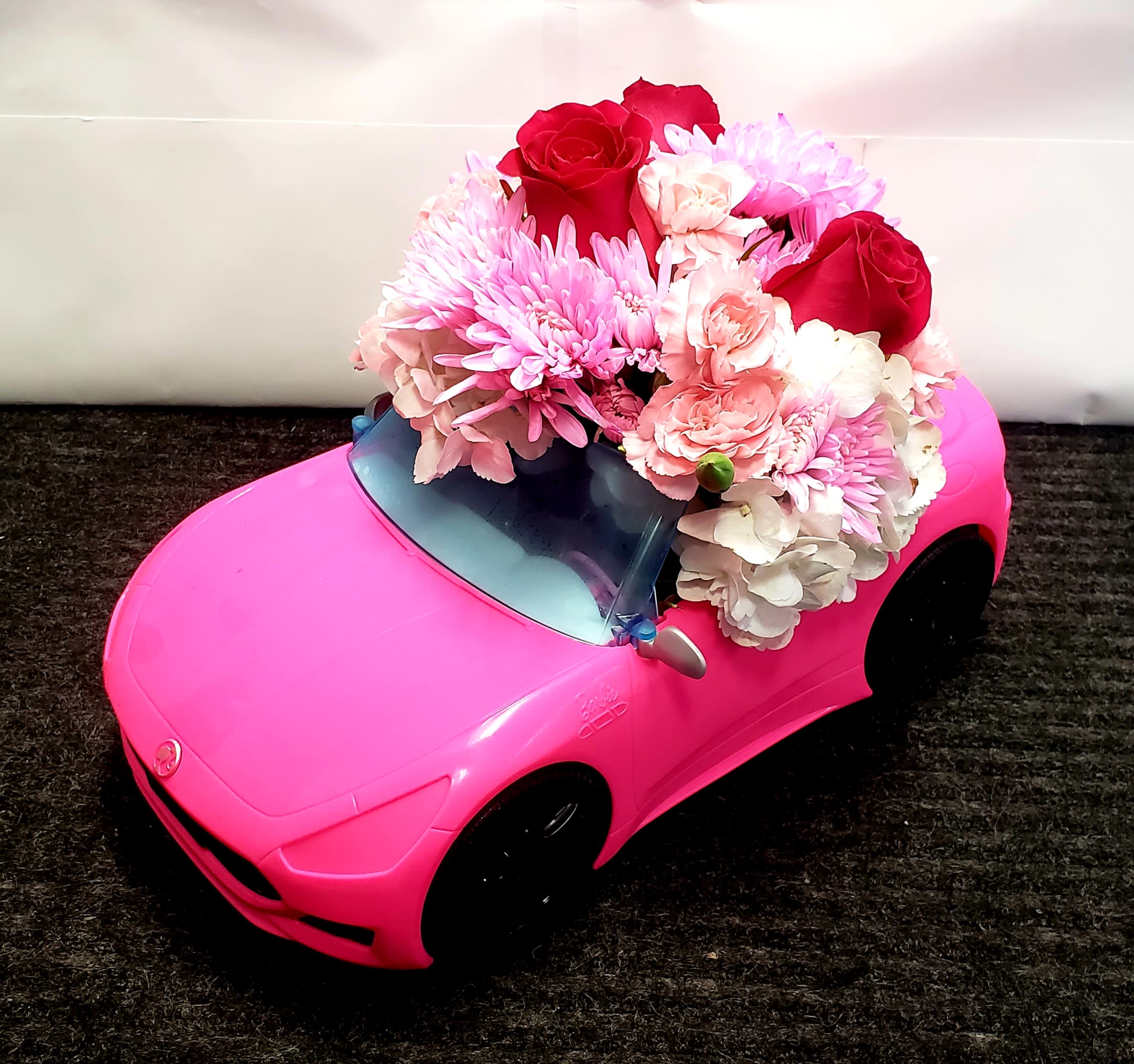 Pink toy car topped with a bouquet of red, pink, and white flowers