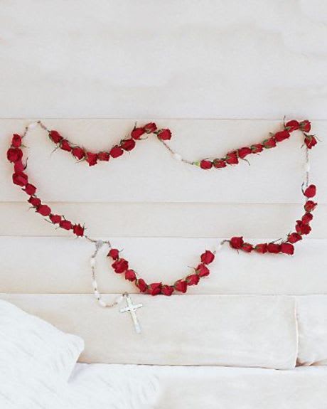Red rose garland draped across a white upholstered headboard with a rosary hanging below