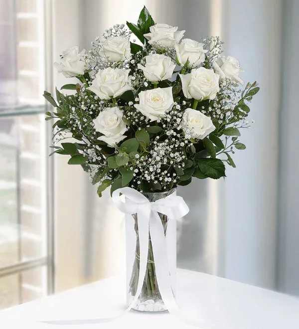 White roses arranged in a clear vase with a white ribbon.