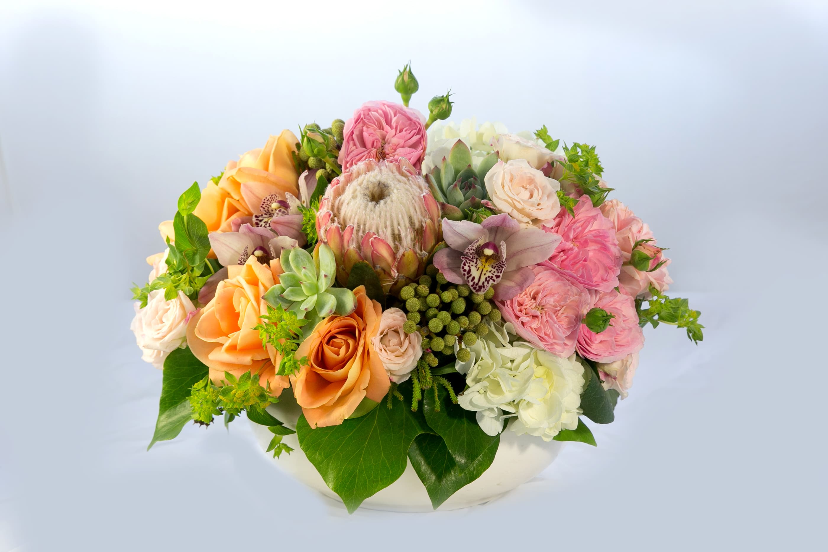 Mixed bouquet of peach, pink, and white flowers in a low white container