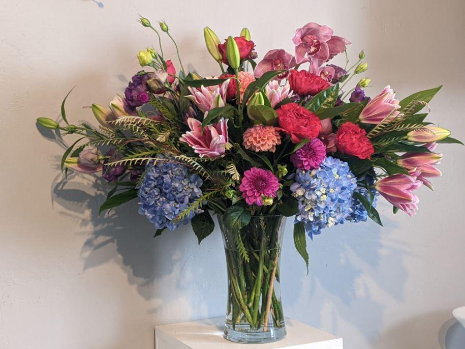 Mixed bouquet of pink, purple, and blue flowers in a clear glass vase