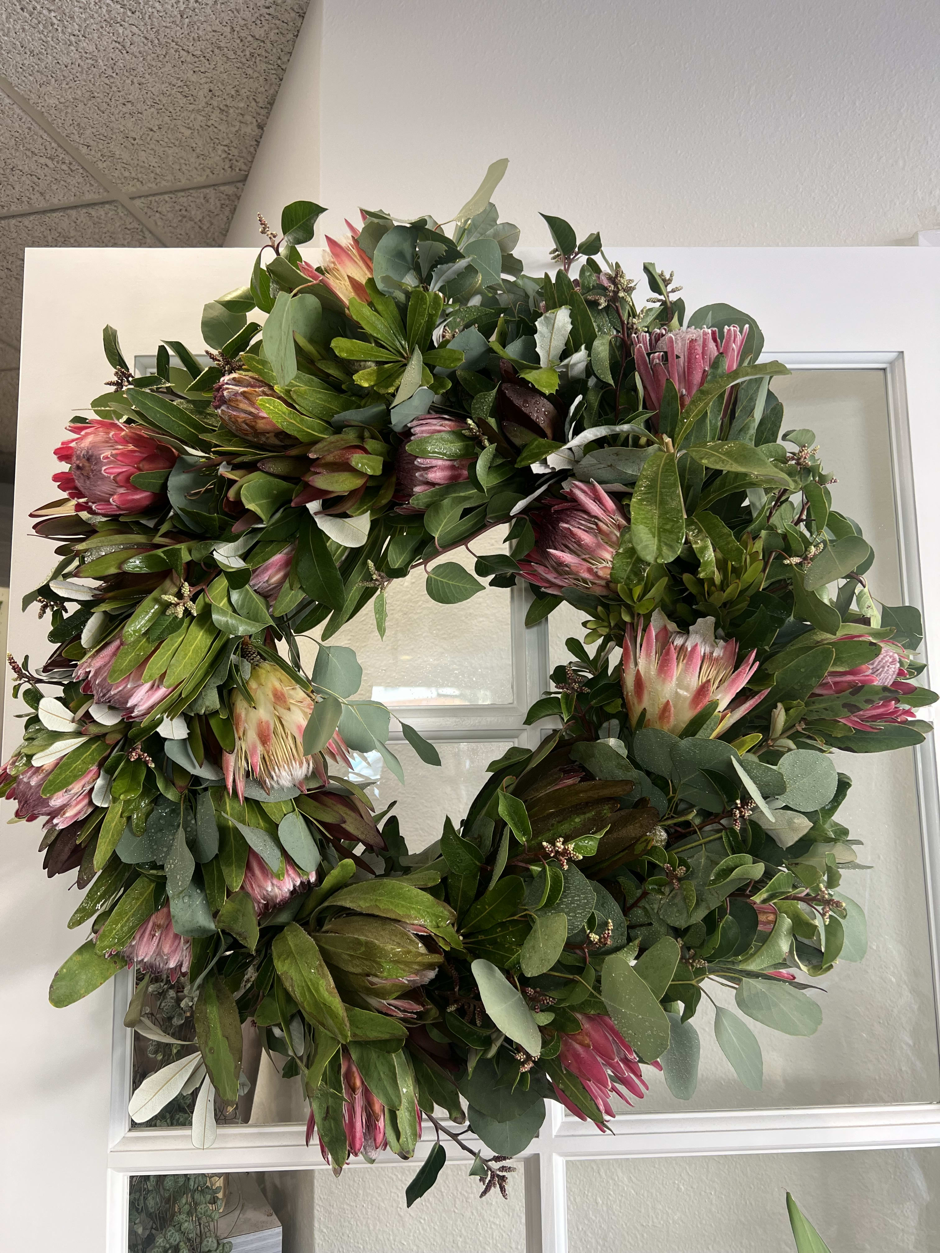 Large wreath with pink protea and mixed greenery on a white door