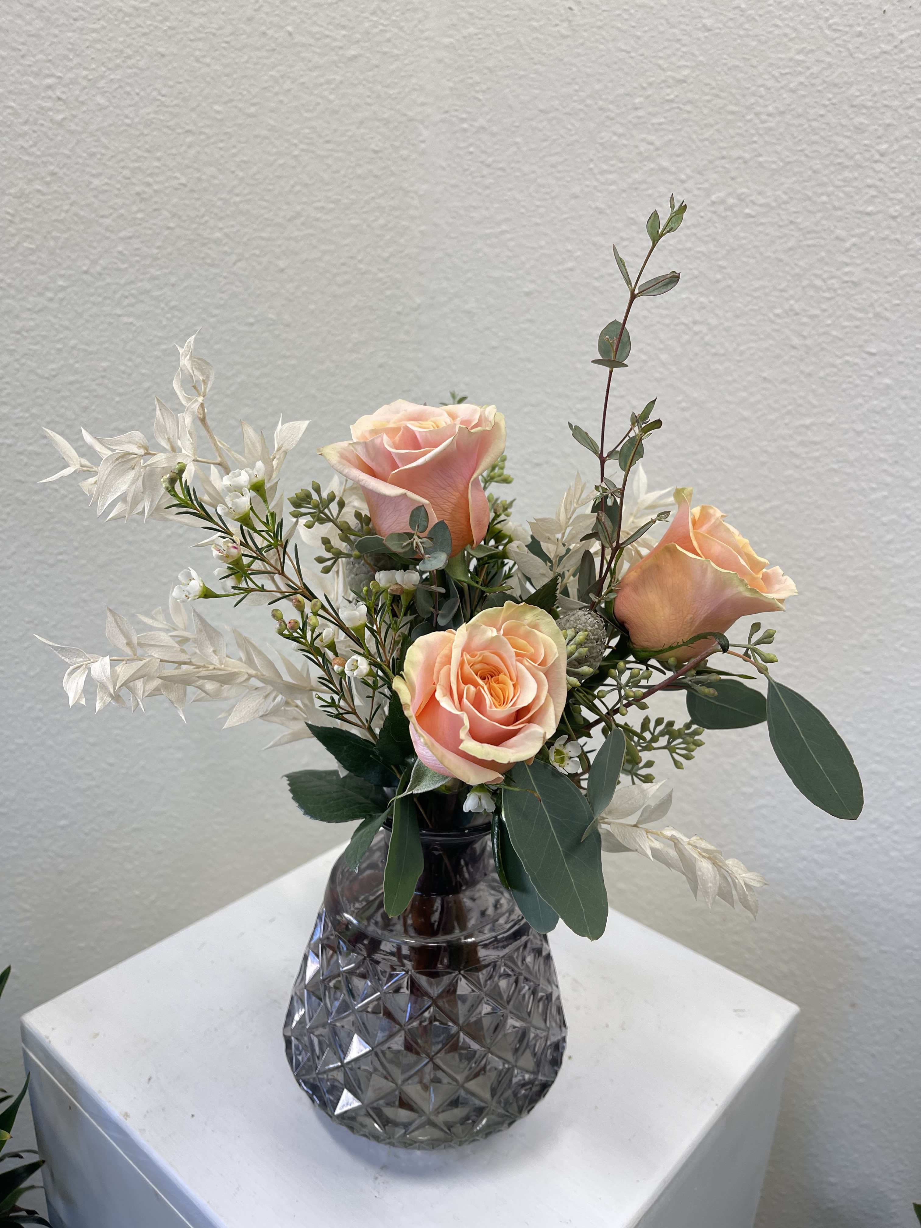 Peach roses in a dark glass vase with white filler flowers