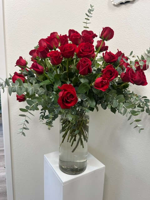 Red roses arranged in a clear glass vase with eucalyptus