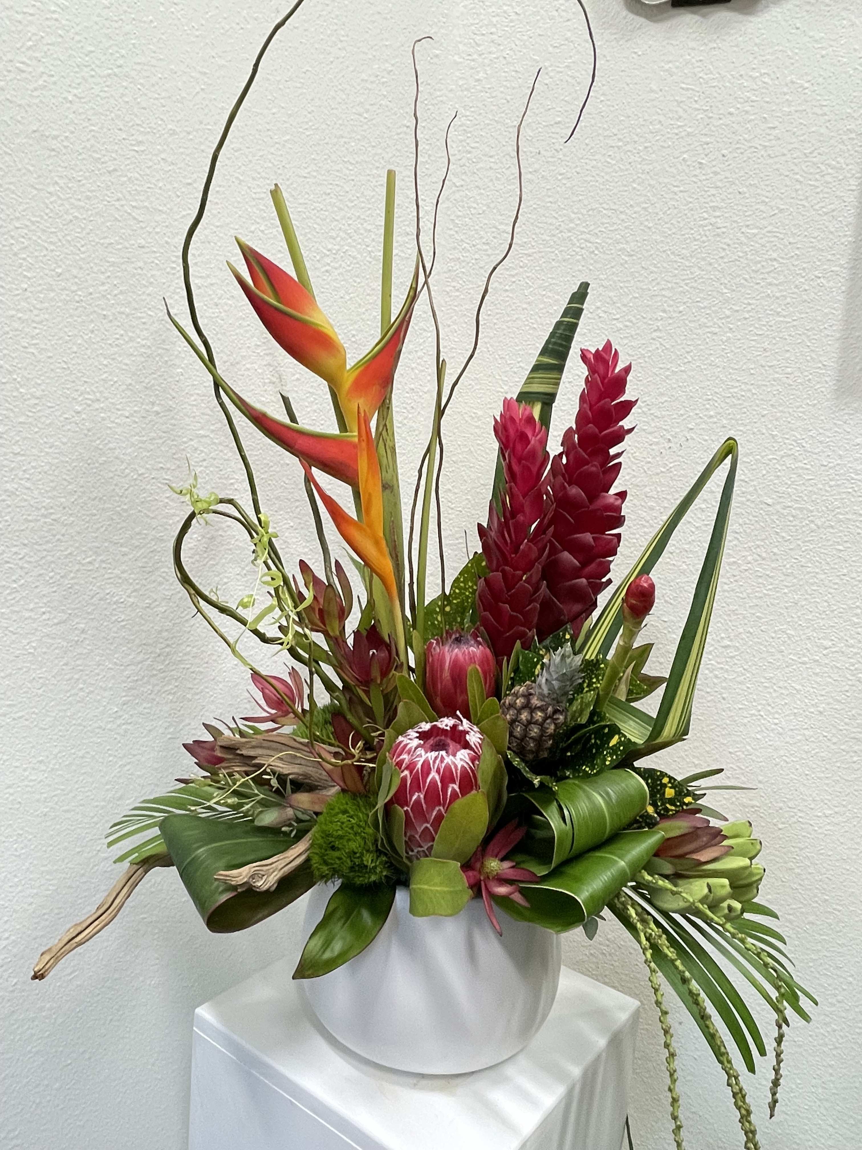 Tropical floral arrangement with red and orange blooms in a white vase