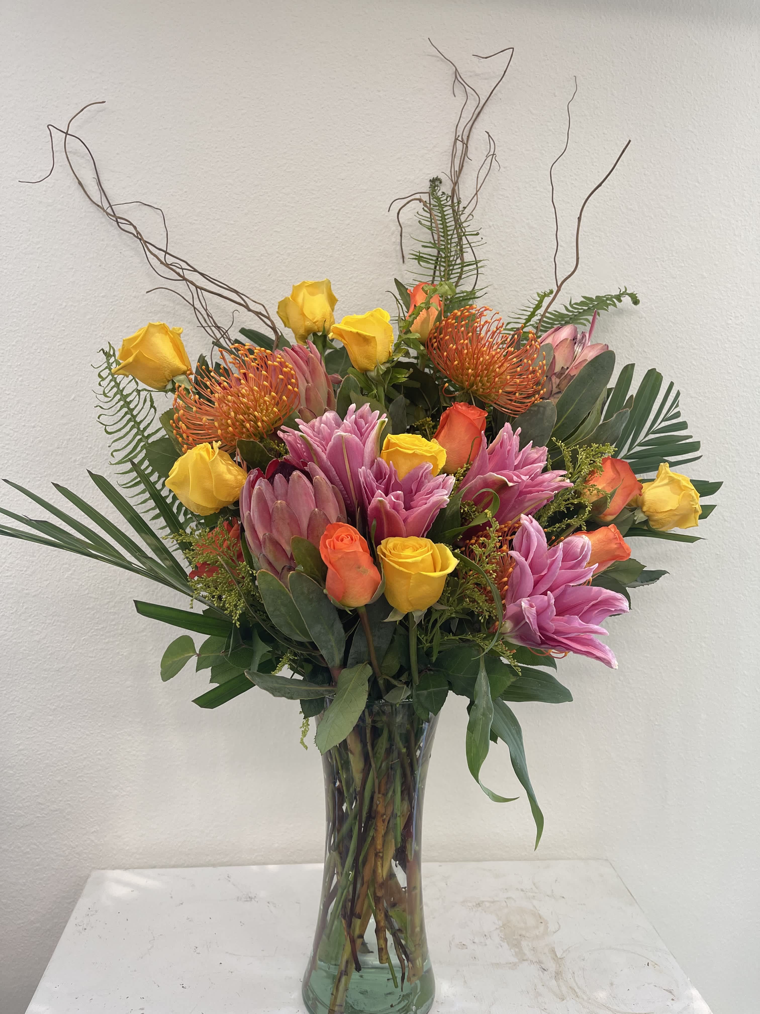 Tall mixed bouquet in a glass vase with yellow and orange roses and pink tropical blooms