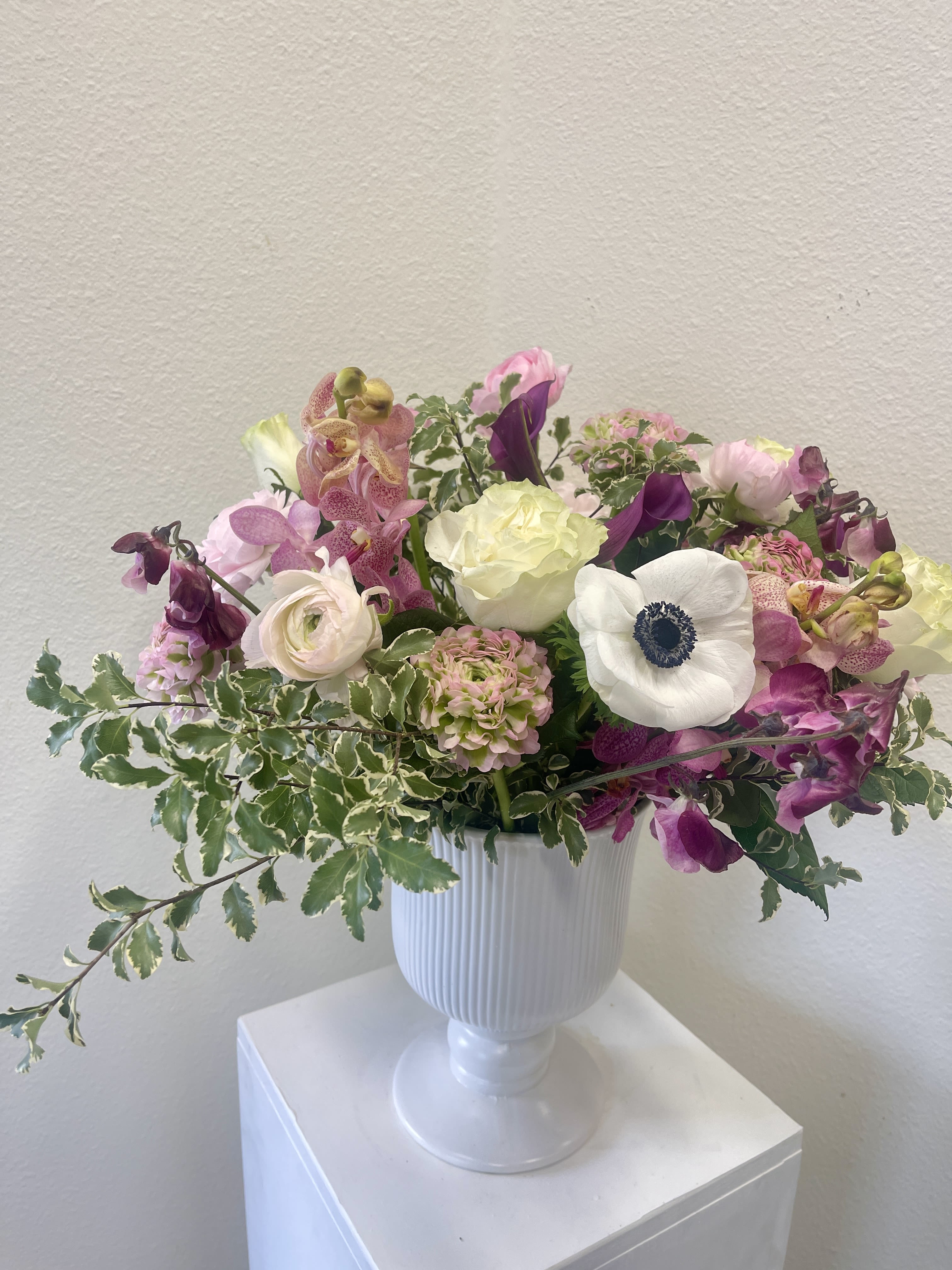 Mixed pink and white flowers arranged in a white pedestal vase