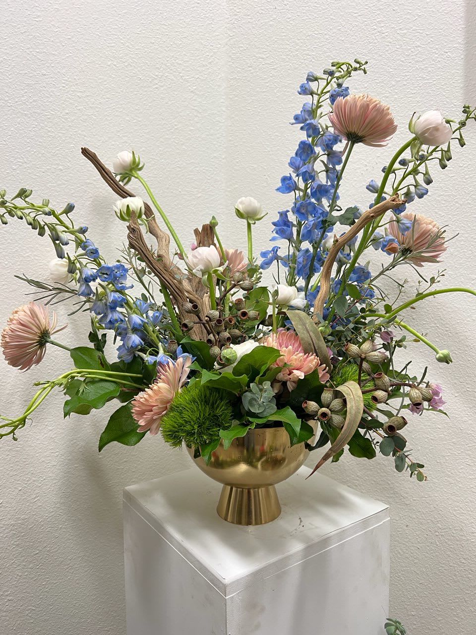 Mixed floral arrangement in a gold vase with blue and blush blooms