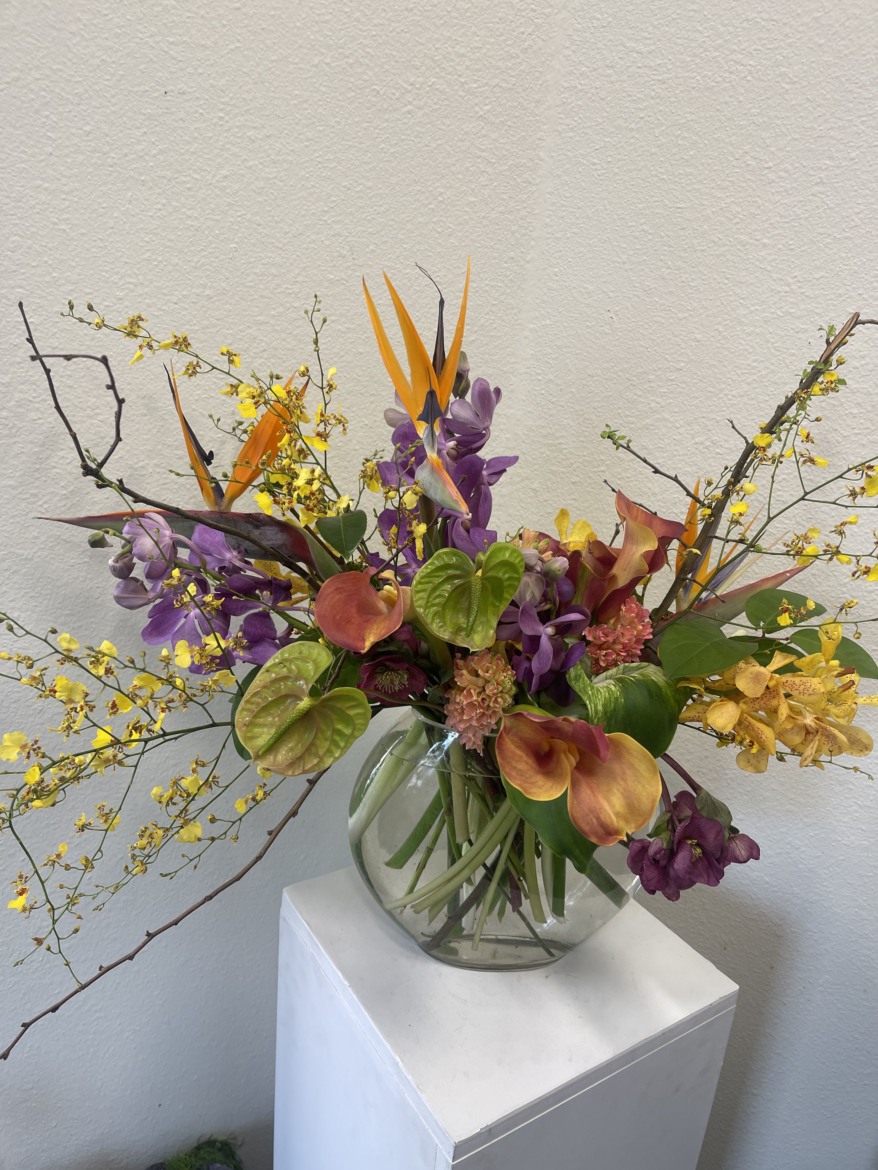 Mixed tropical bouquet in a clear glass vase with orange bird-of-paradise and purple orchids