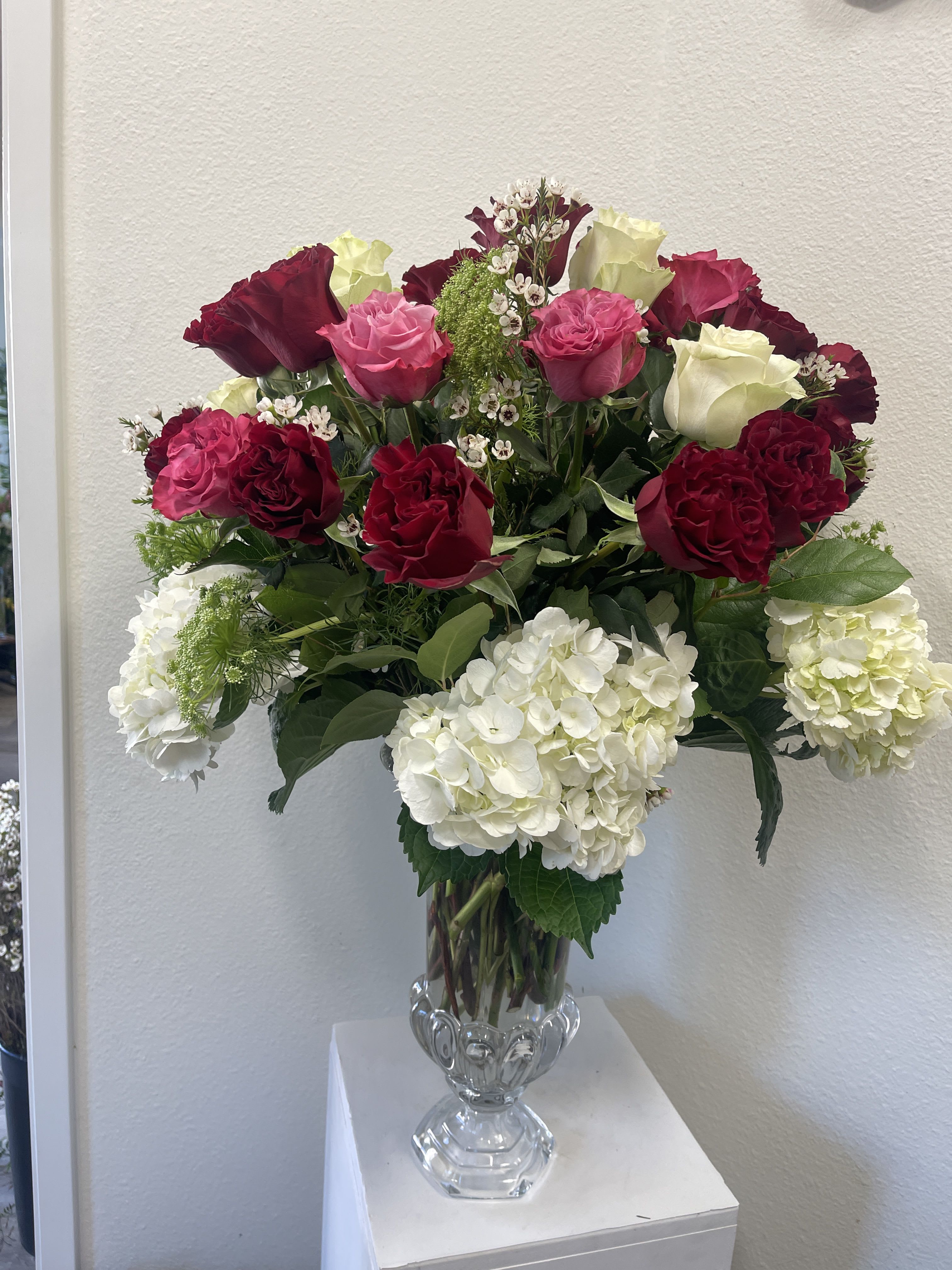 Tall glass vase with white hydrangeas and red, pink, and cream roses in a mixed arrangement