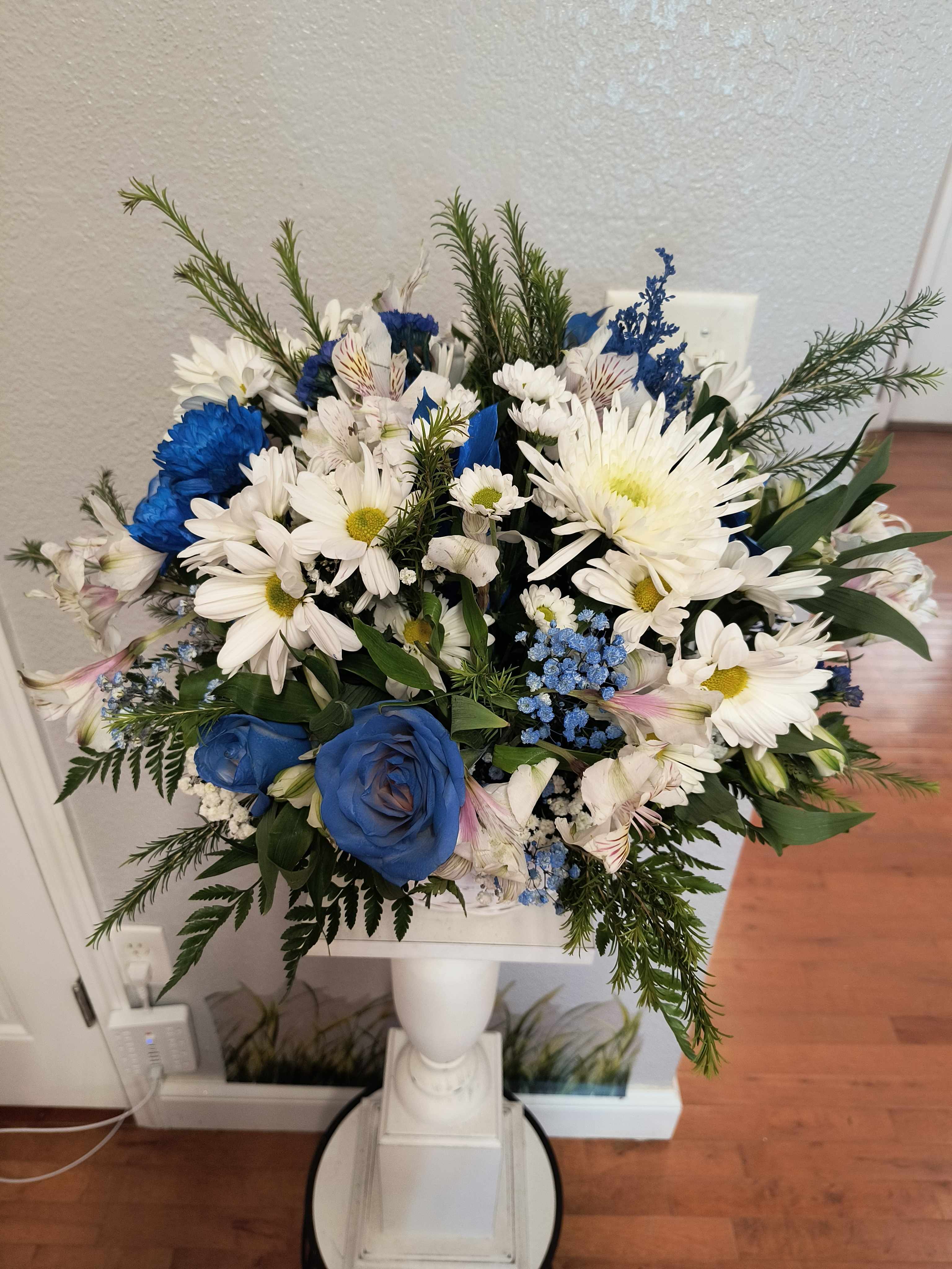 Blue and white mixed flower arrangement in a white pedestal vase