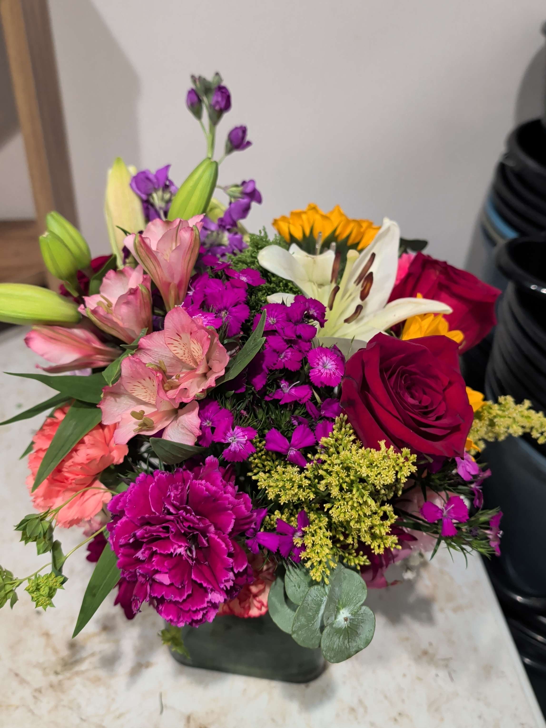 Mixed bouquet with roses, lilies, carnations, and purple filler flowers in a vase