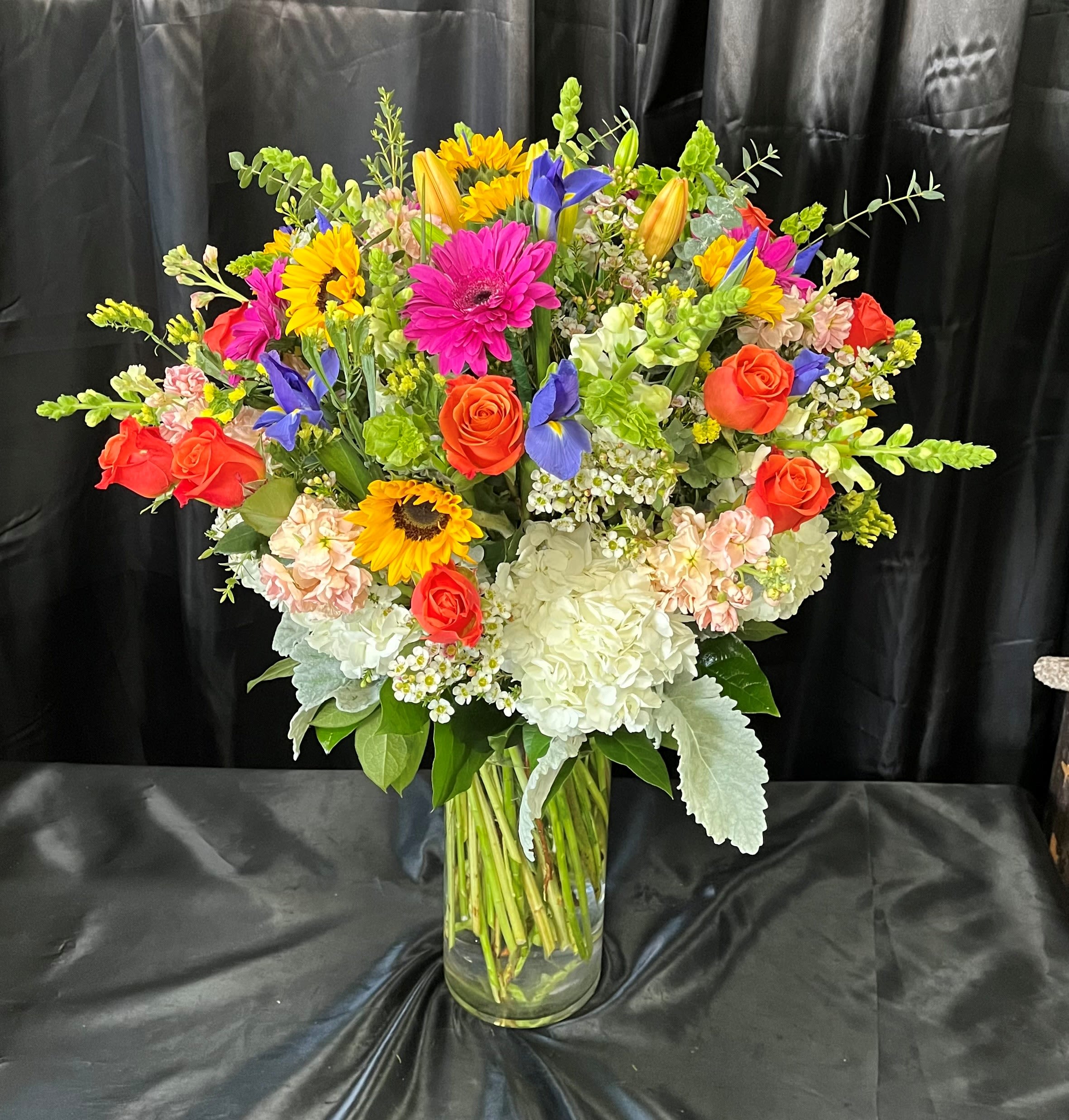 Mixed bouquet of roses, sunflowers, hydrangeas, and irises in a glass vase