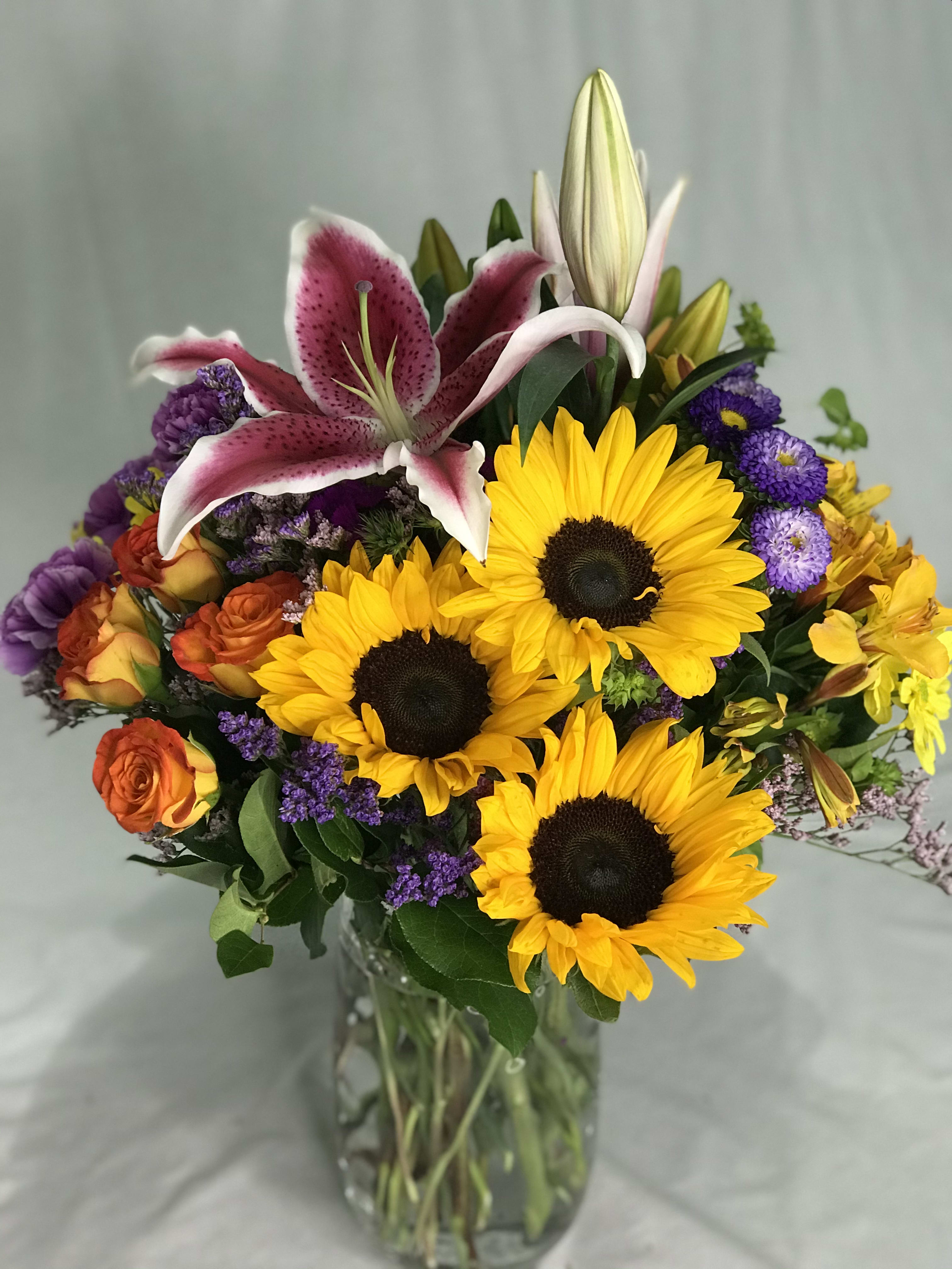 Bouquet of sunflowers, lilies, and roses in a glass vase
