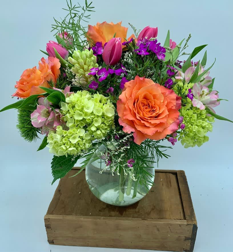 Mixed bouquet of orange roses, pink tulips, and green hydrangeas in a glass vase
