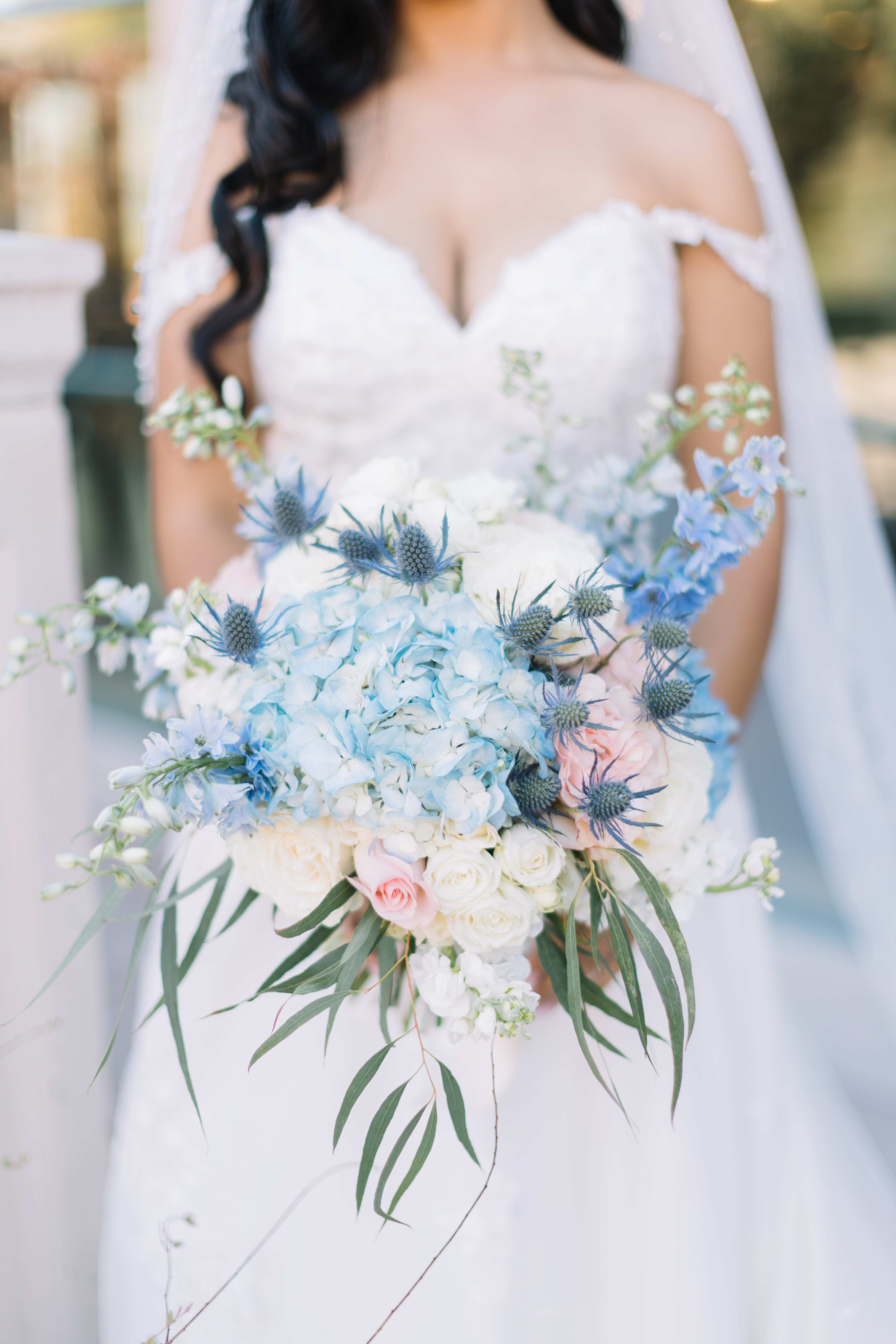 Bride holding a pastel blue and white bouquet with roses and thistle