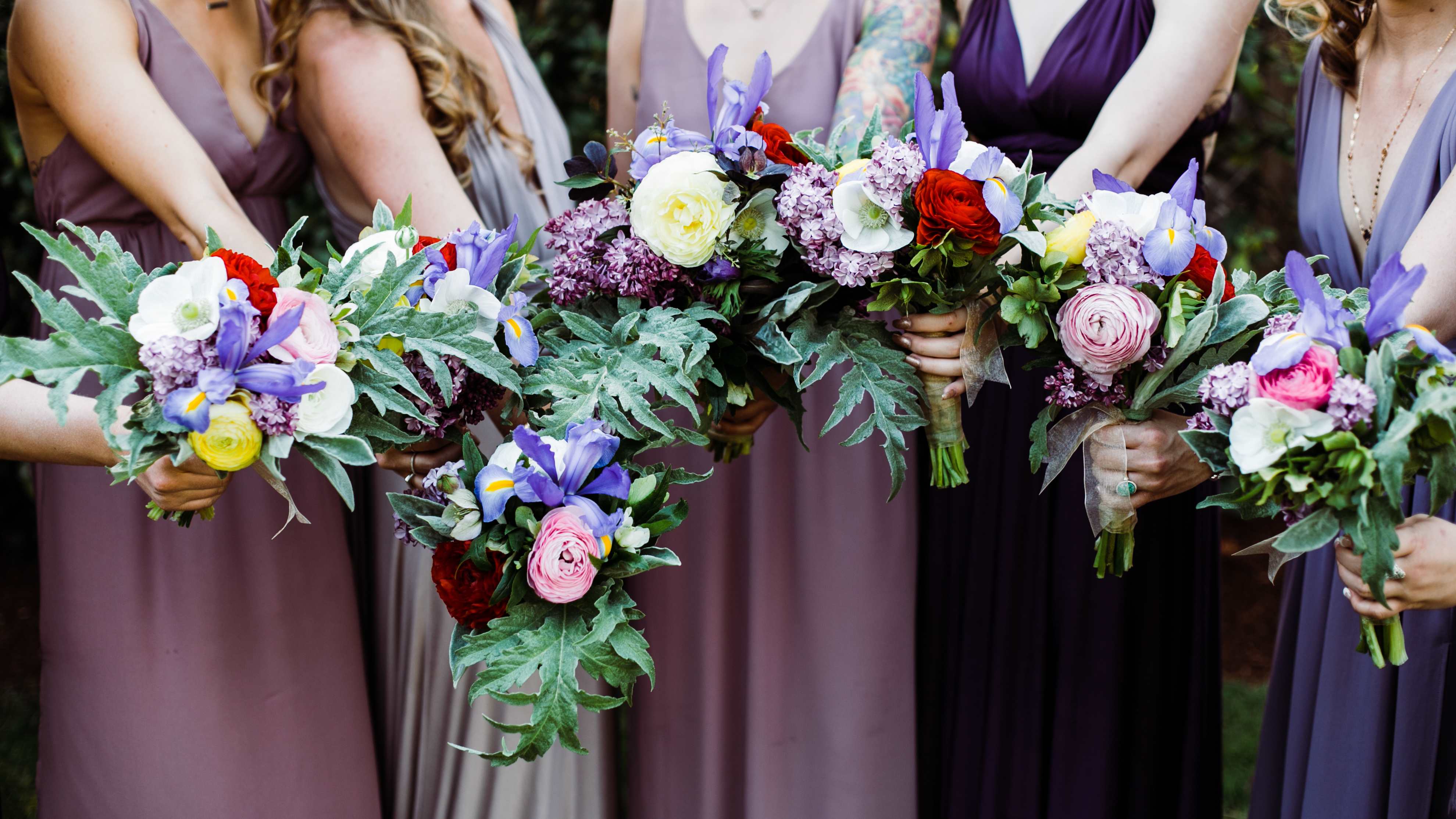 Bridesmaids holding colorful bouquets with purple, pink, white, and red flowers
