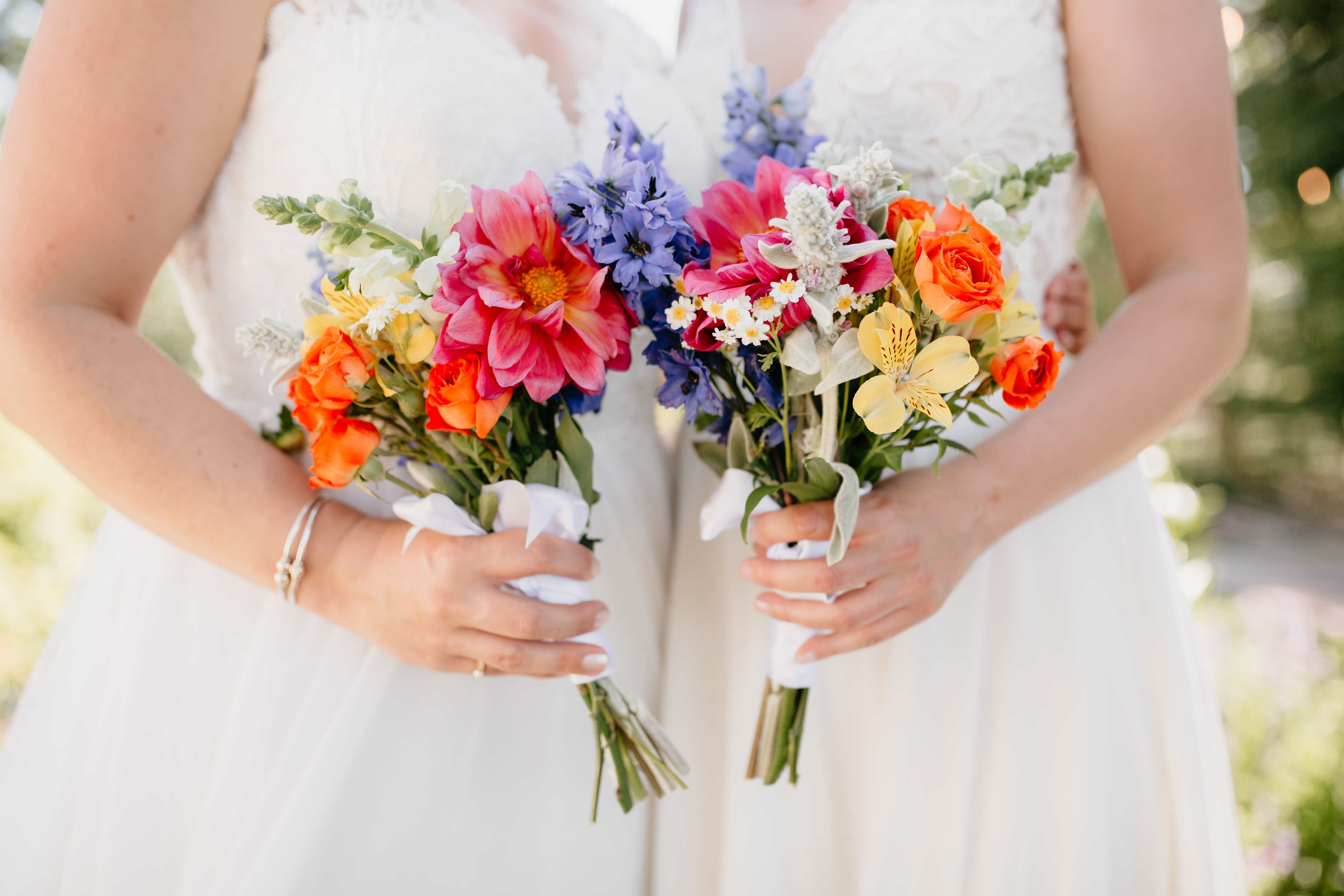 Bride holding two colorful bouquets with pink, orange, blue, and yellow flowers