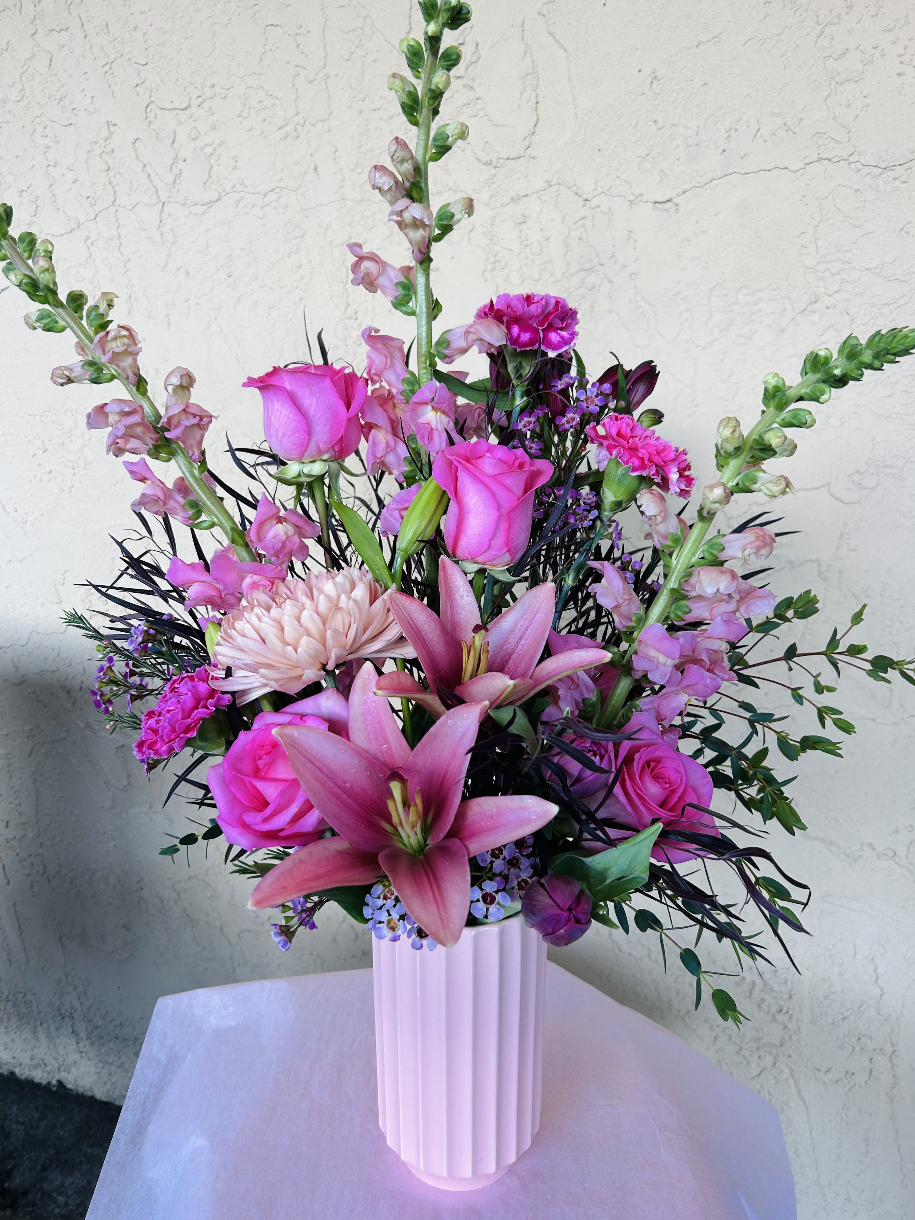 Pink roses and lilies in a white vase with purple accents