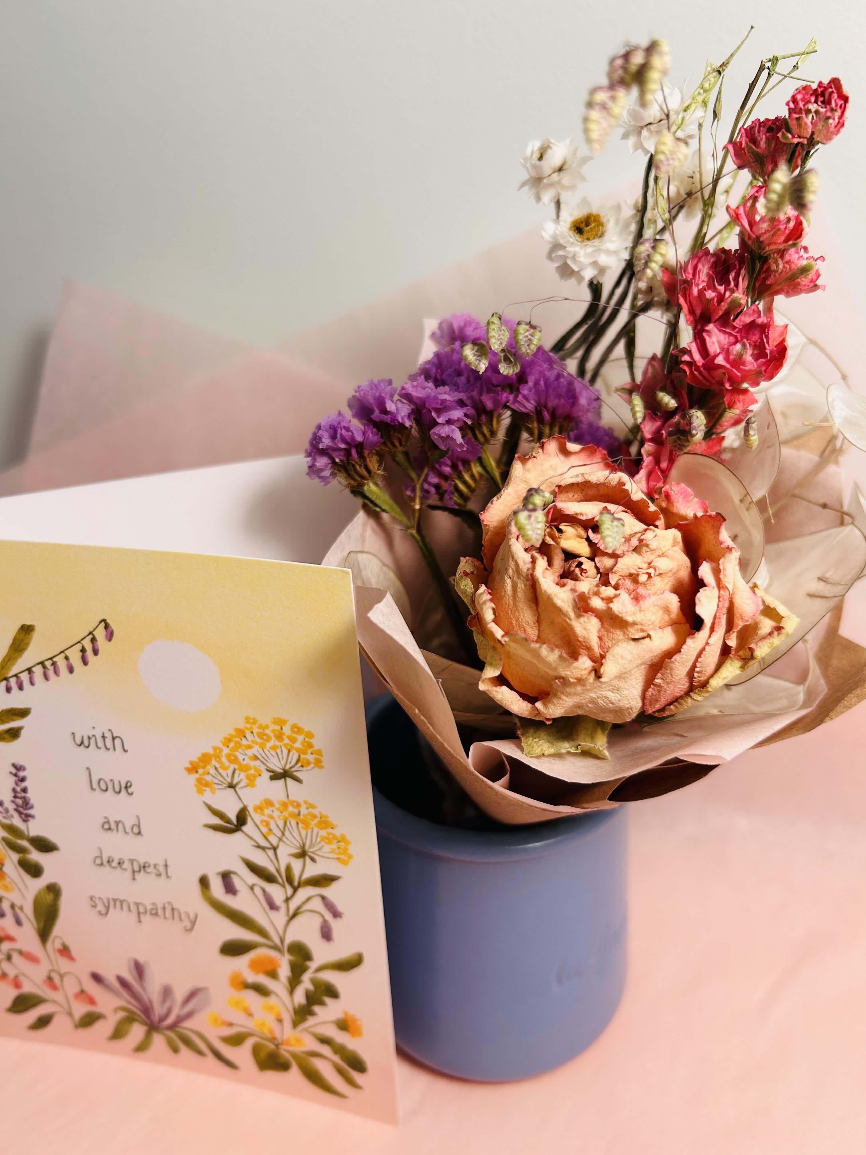Bouquet of dried flowers in a blue vase beside a sympathy card
