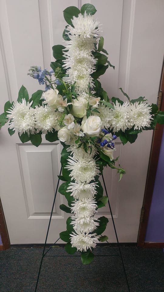 White floral cross on a stand with roses and chrysanthemums