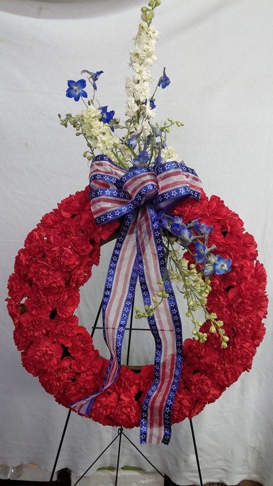 Red floral wreath with blue and white flowers and an American flag ribbon
