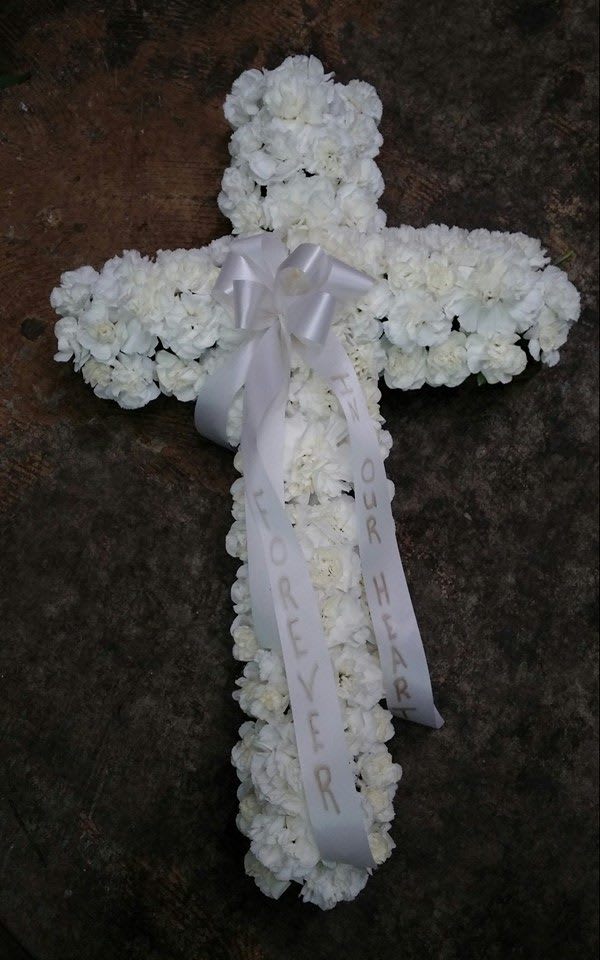 White floral cross with a ribbon bow and hanging memorial ribbons