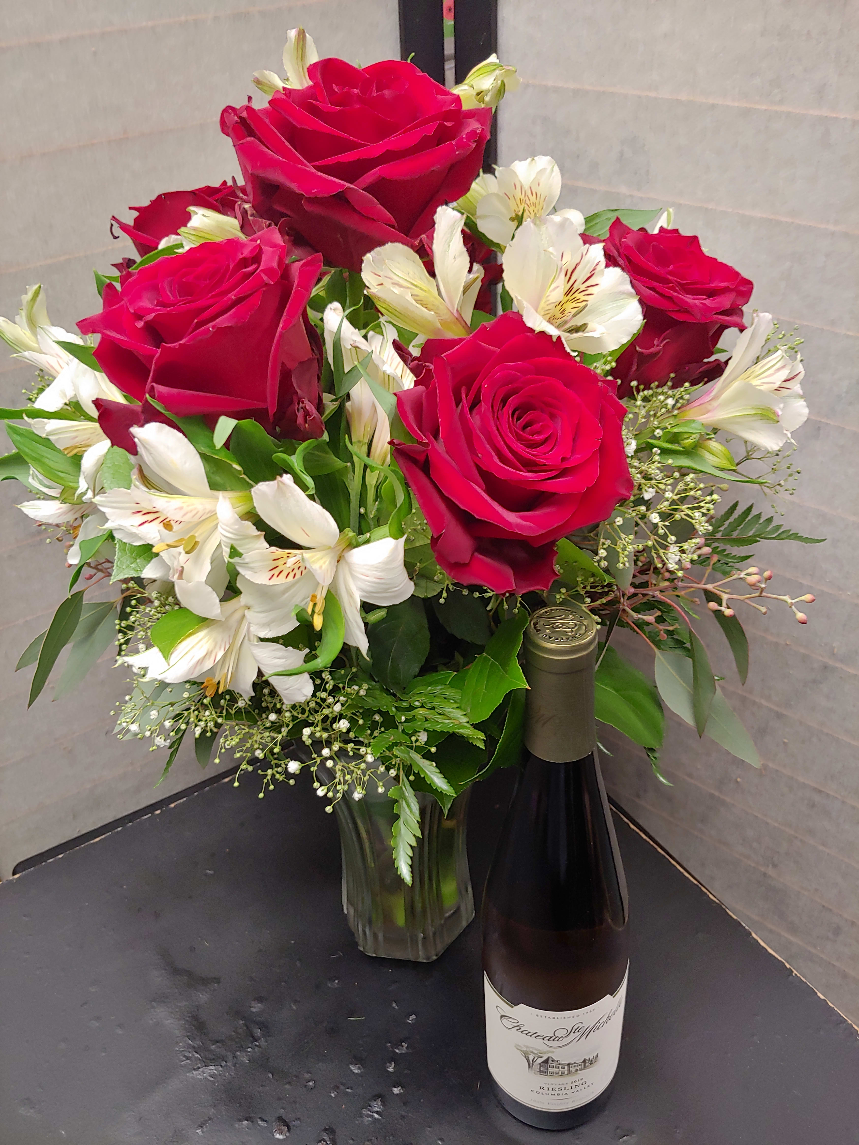 Bouquet of red roses and white alstroemeria in a glass vase with a wine bottle