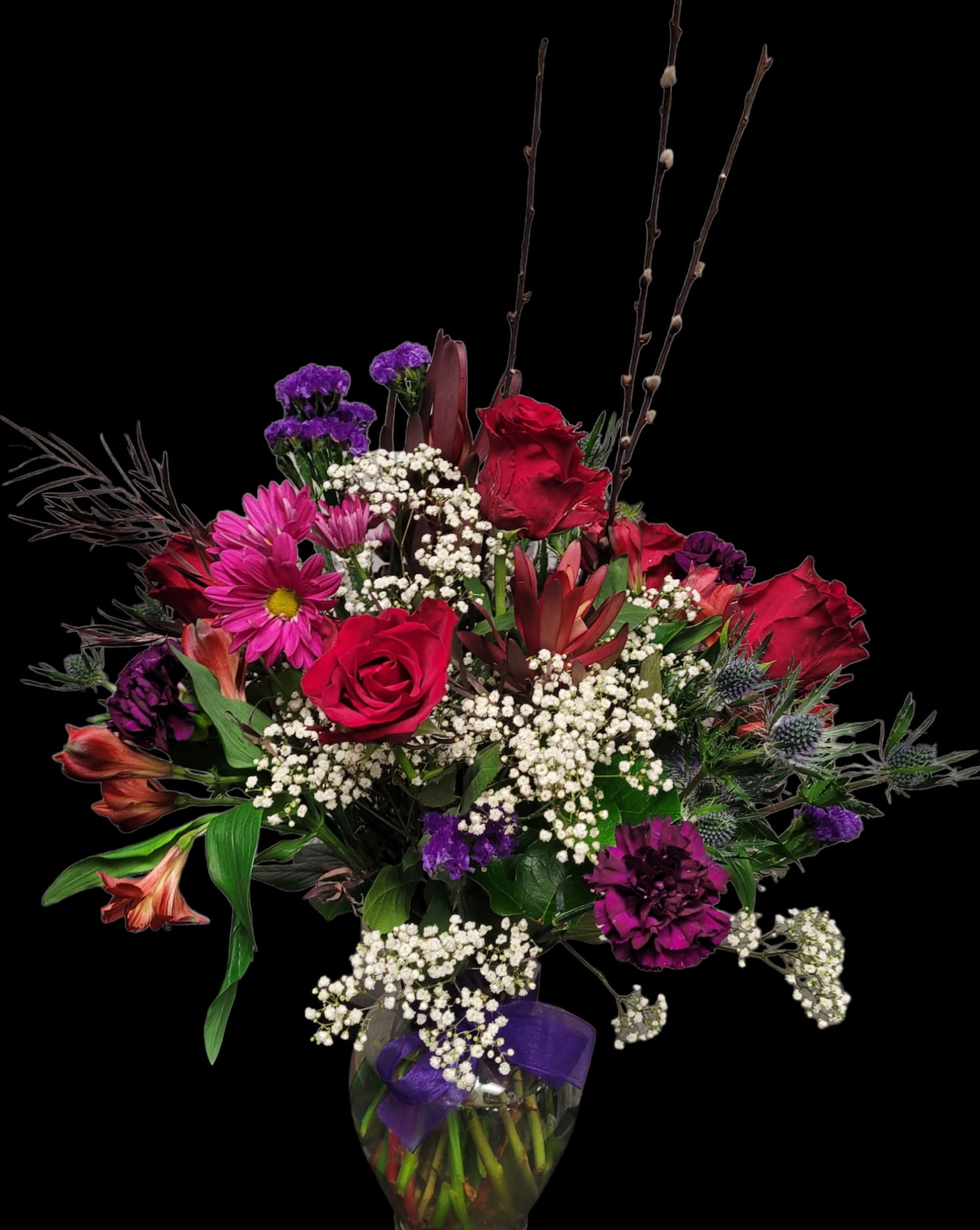 Bouquet of red roses, purple blooms, and white baby's breath in a glass vase