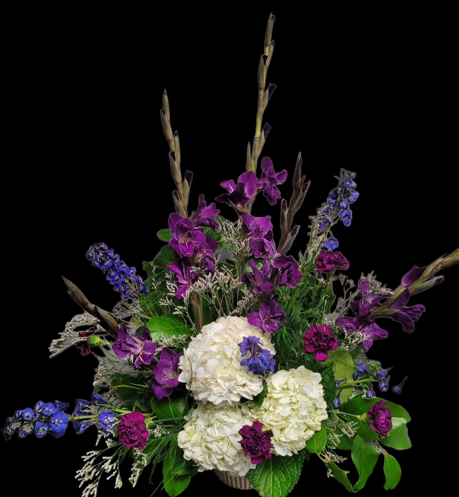 Purple and blue flowers arranged with white hydrangeas in a vase
