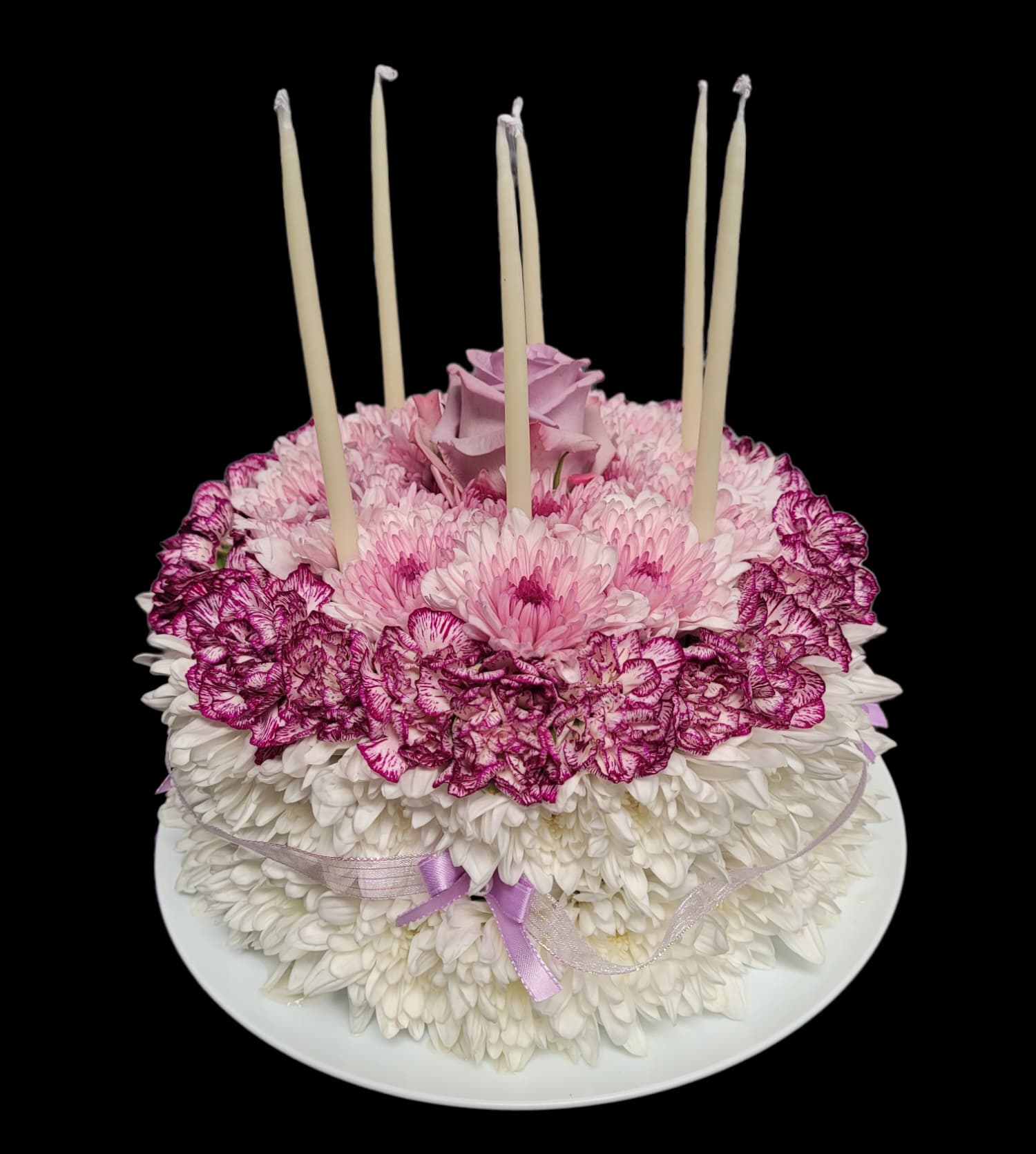 Round floral cake with pink and white flowers and tall candles