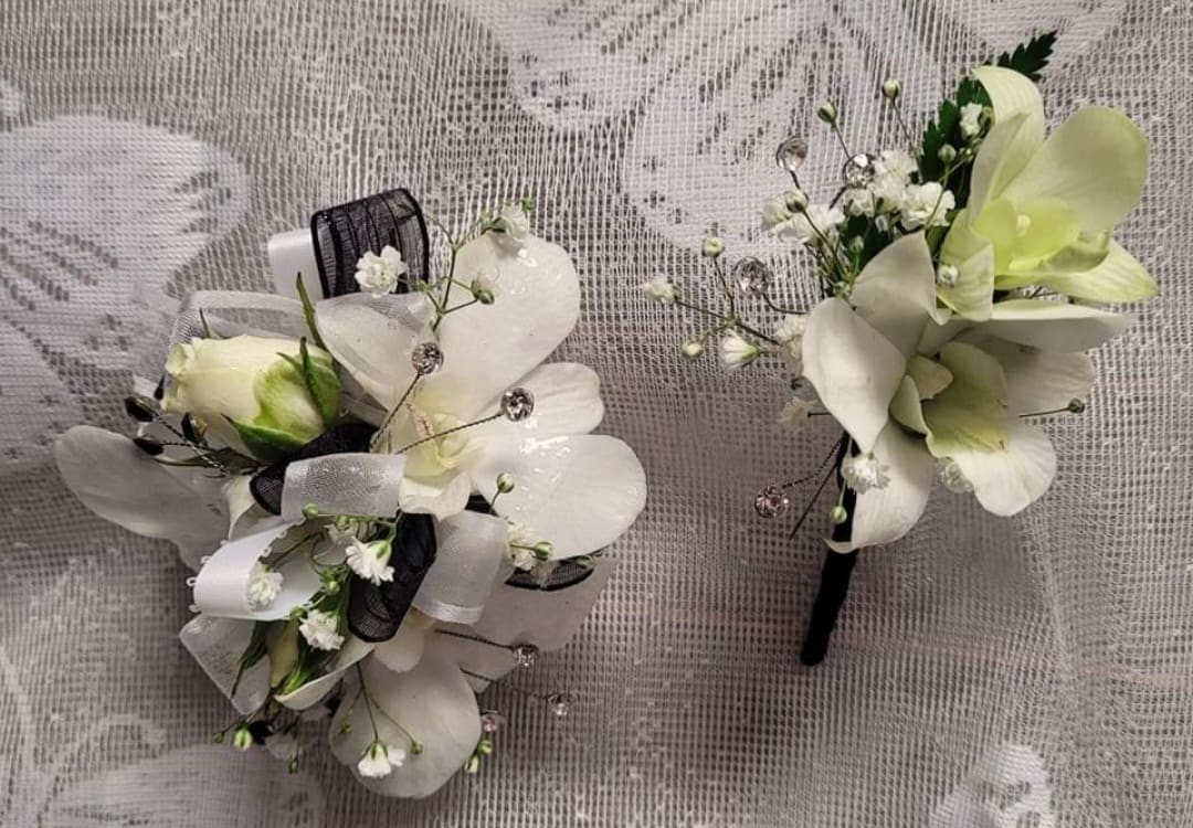Two white orchid boutonnieres with black and white ribbon accents