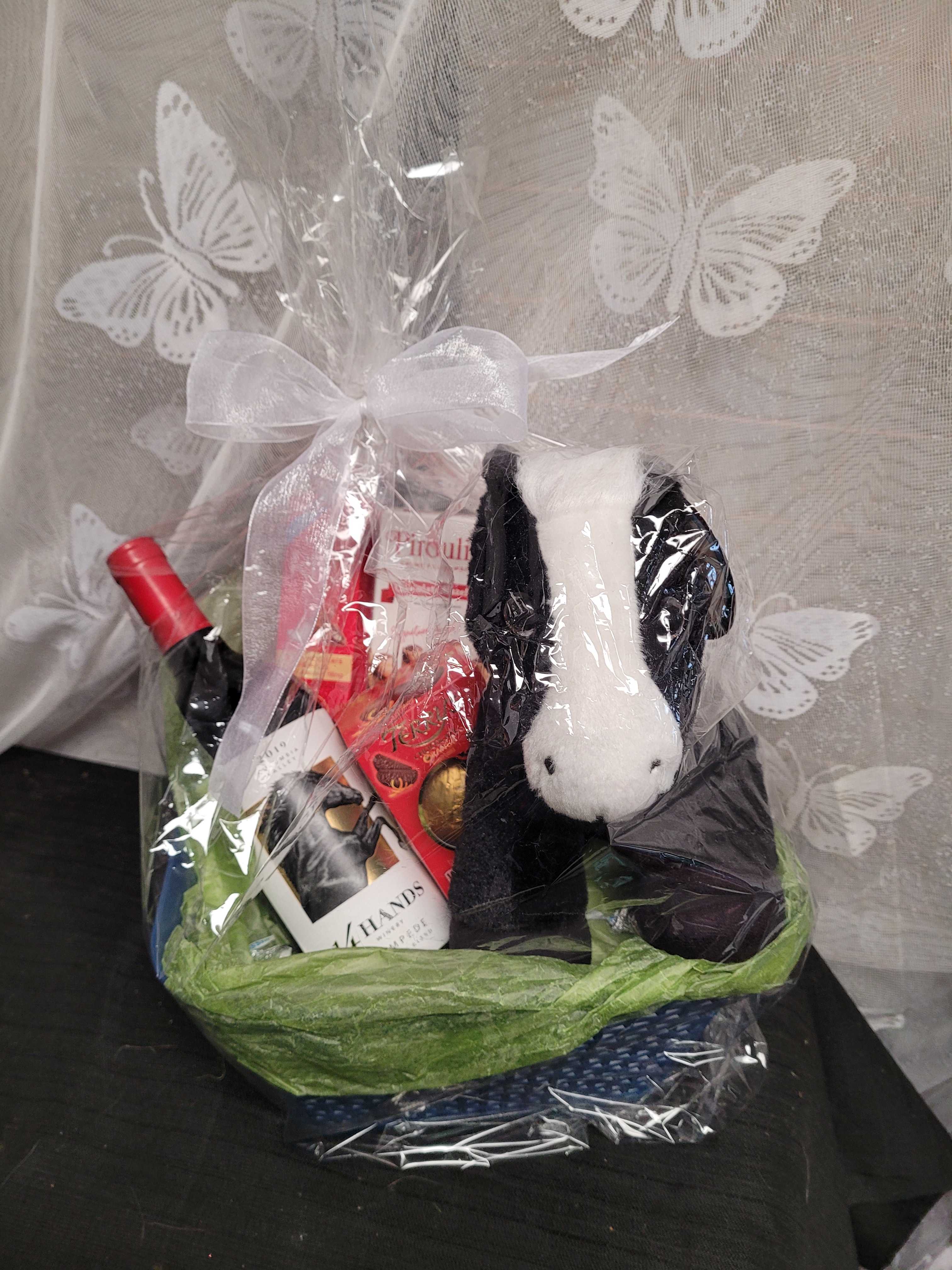 Gift basket with wine, chocolates, and a plush dog in clear wrap